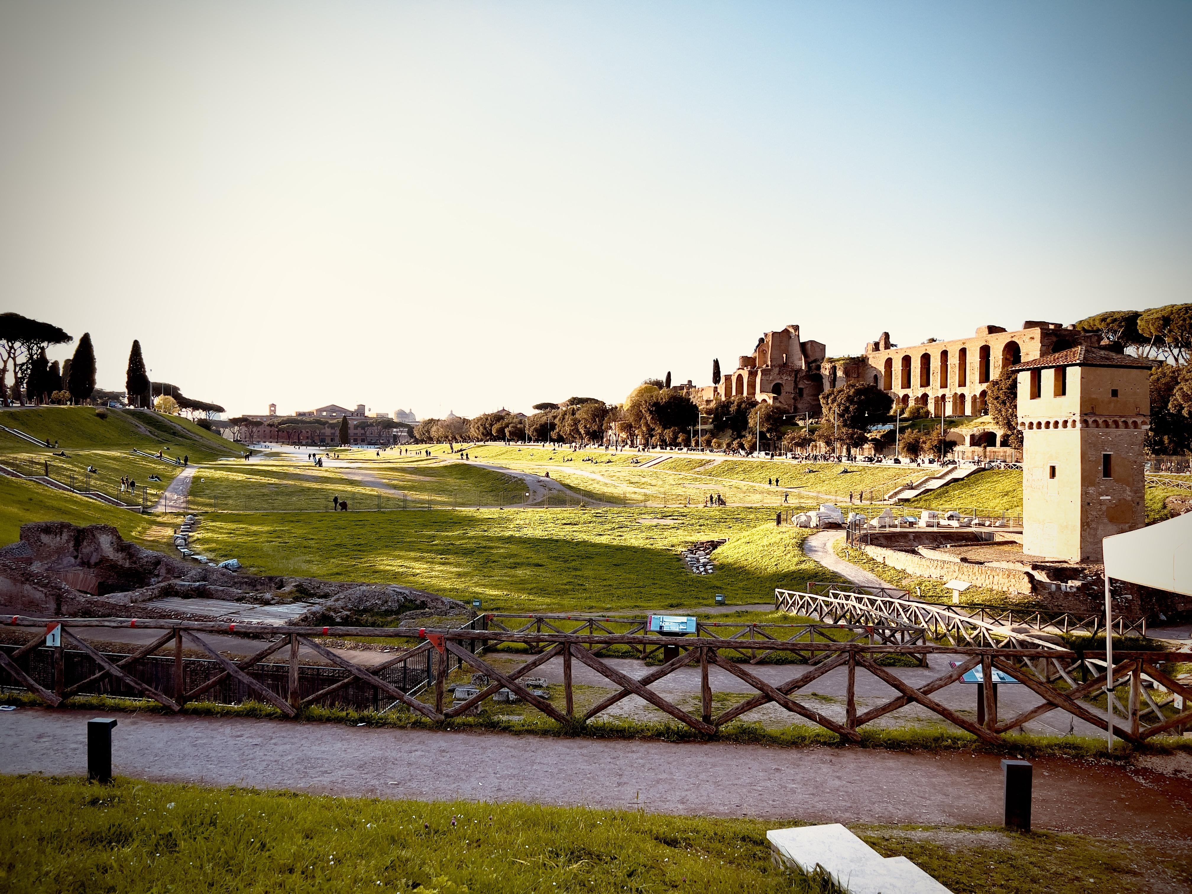 Circo Massimo a Roma, Italia. È un antico stadio romano per corse di carri e luogo di intrattenimento di massa. L’area è ora un parco pubblico con spazi verdi aperti e rovine circostanti. Il Colle Palatino è visibile sullo sfondo con le sue strutture storiche.
