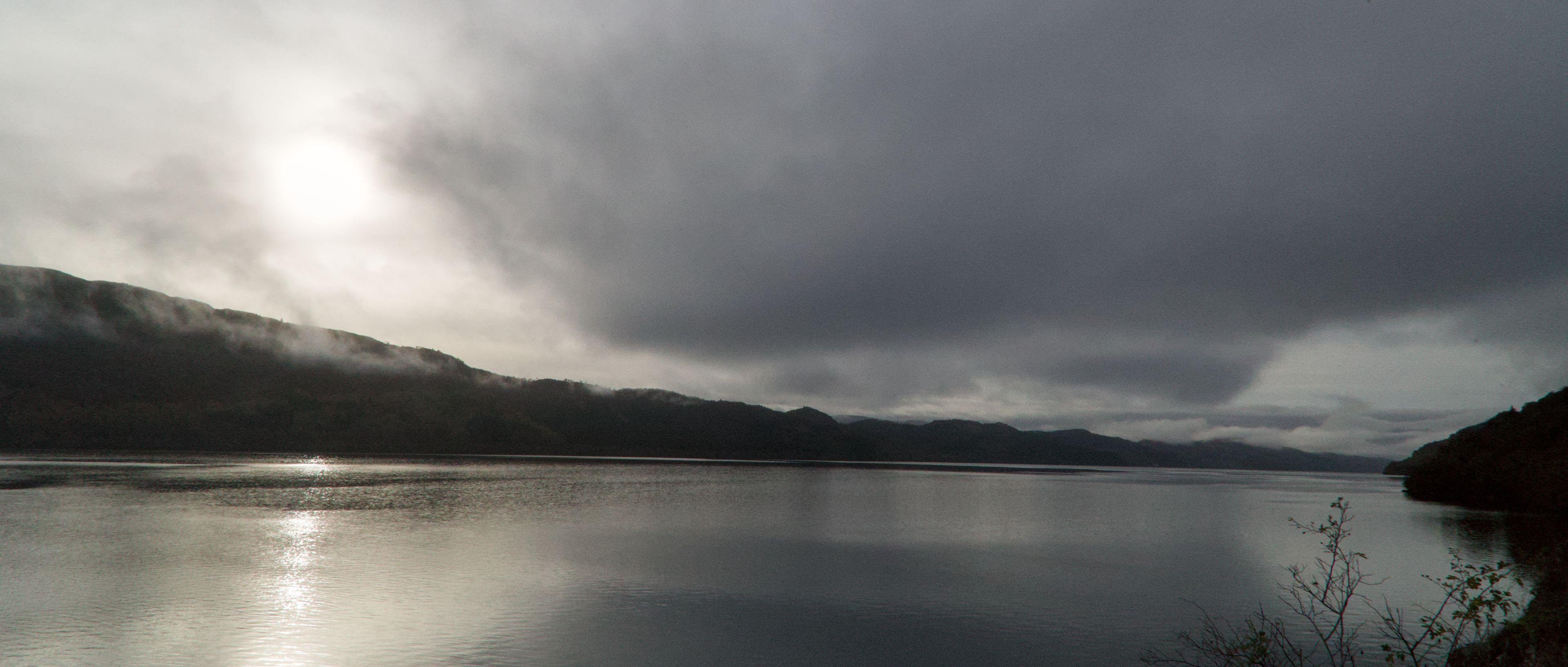 Photo horizontale sur un lac calme, encadré par les highlands sous un ciel chargé