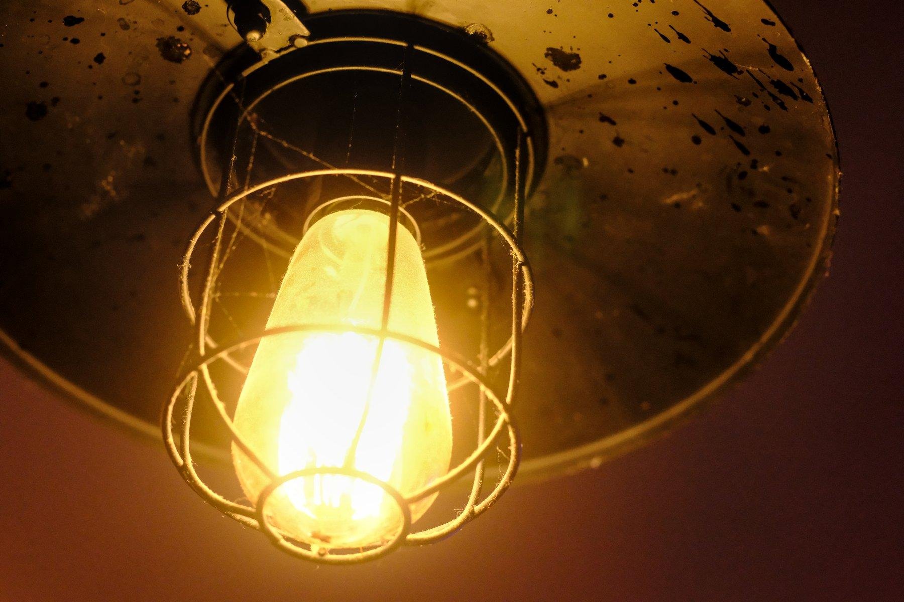 Photo horizontale. Vue contre plongée sur une ampoule orange, dans une cage de protection sous un abat jour en métal