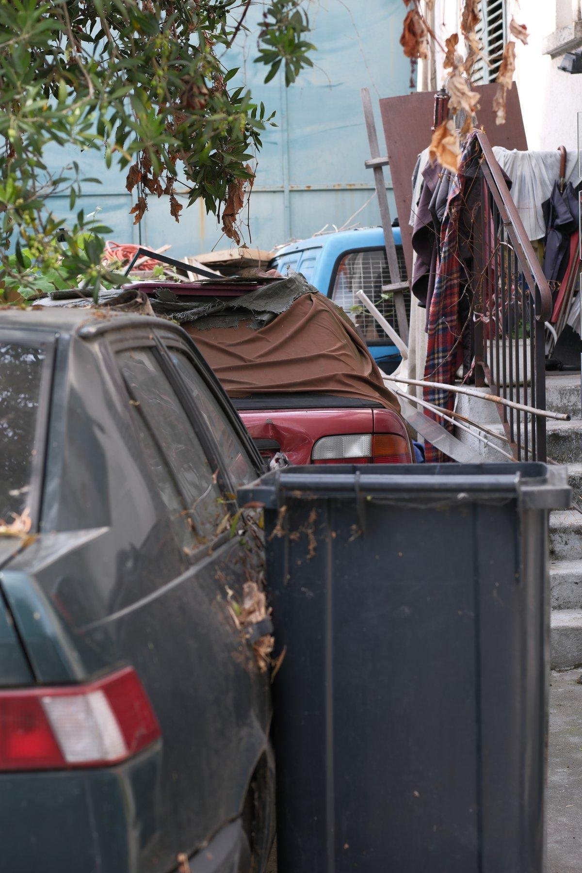 Three abandoned cars, one behind the others, in a small driveway, crumpled by trash and stuff