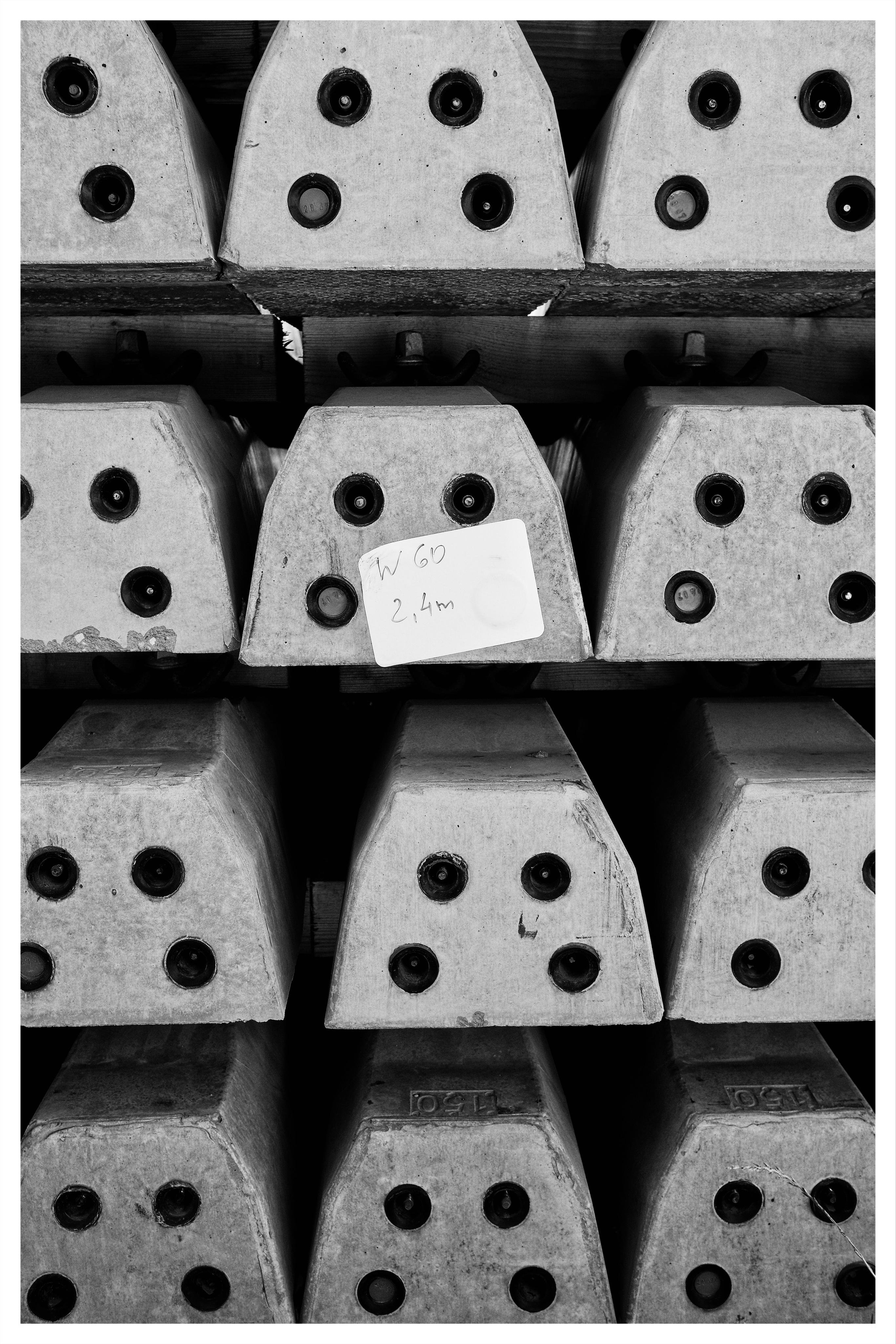 Stacked concrete blocks arranged in rows, each with four circular bolt holes on the end face; a small handwritten label reading “W 60 2.4m” is taped to one block near the center.