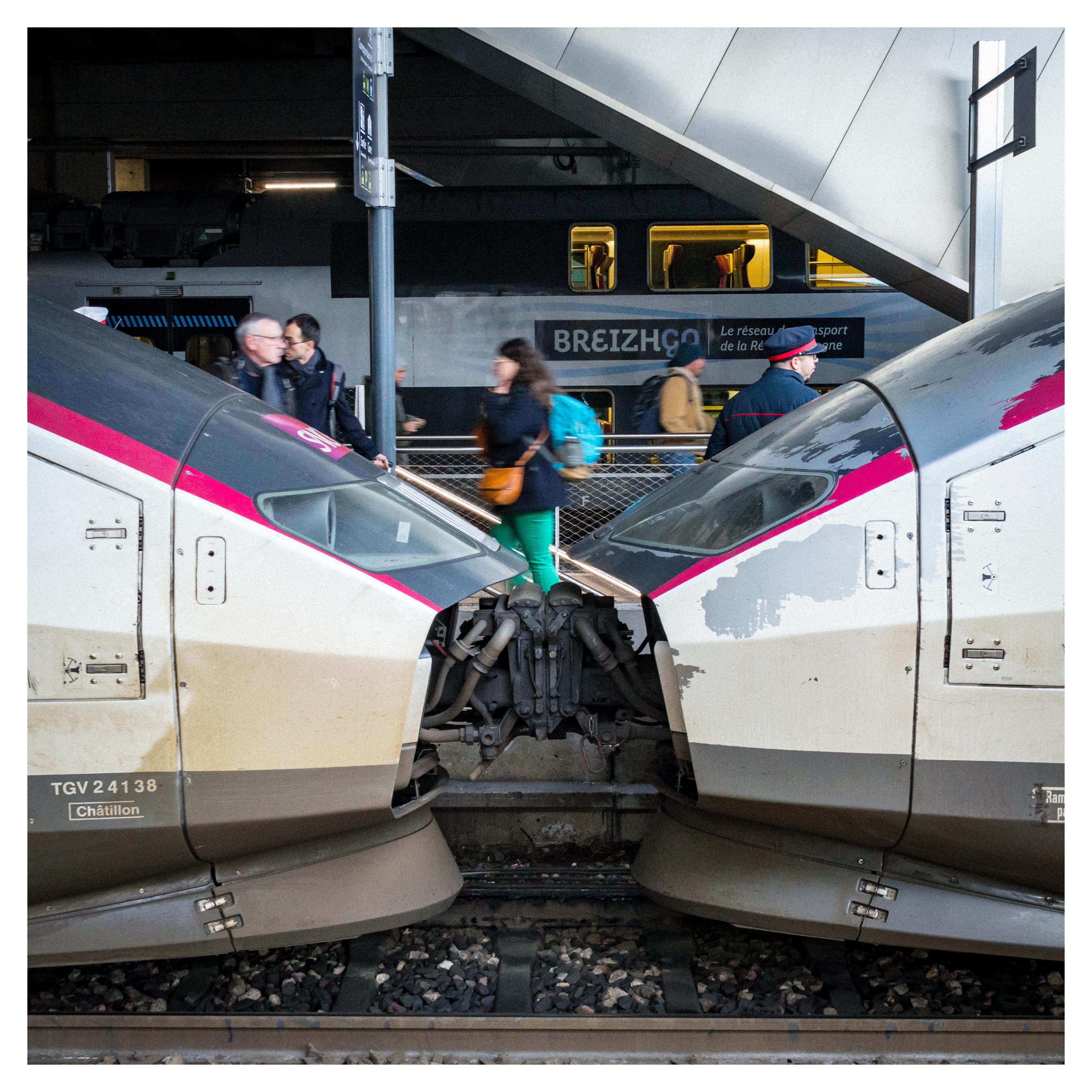 People walking on a platform of Rennes station with two TGV trains in between them and the camera
