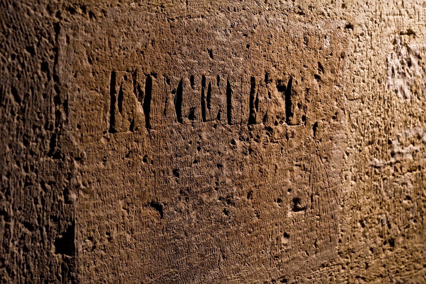 A stonewall lit by an orange light where a name is carved in capital letters, reading “EICEILL” (approx)