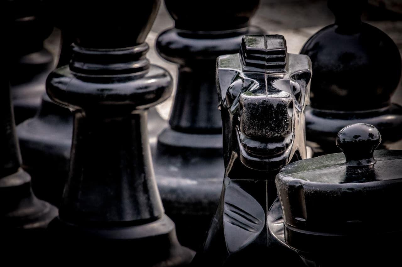 The image shows large black chess pieces, including a prominent knight in the foreground.