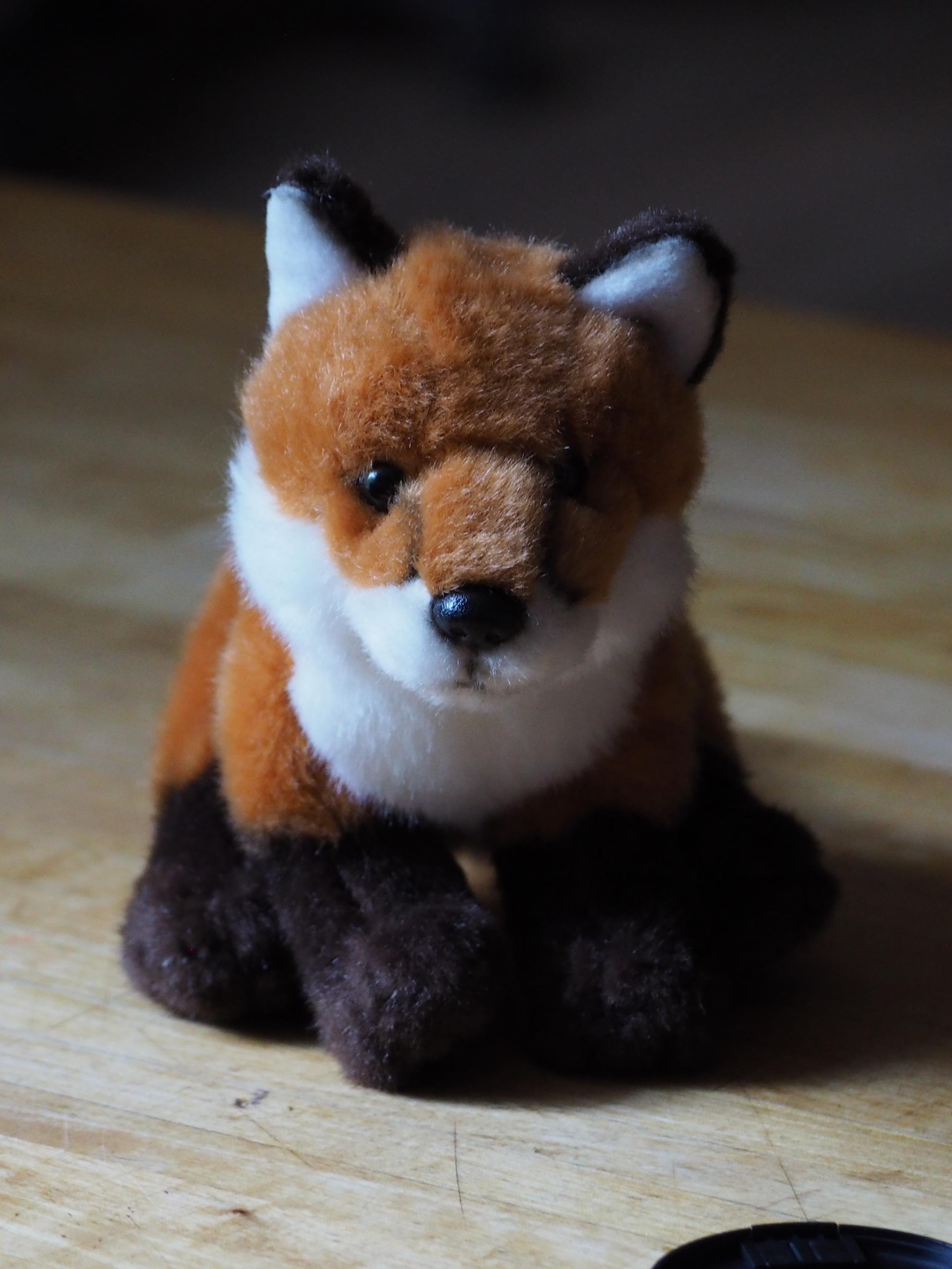 A plush fox toy with orange, white, and dark brown fur, sitting on a wooden surface.