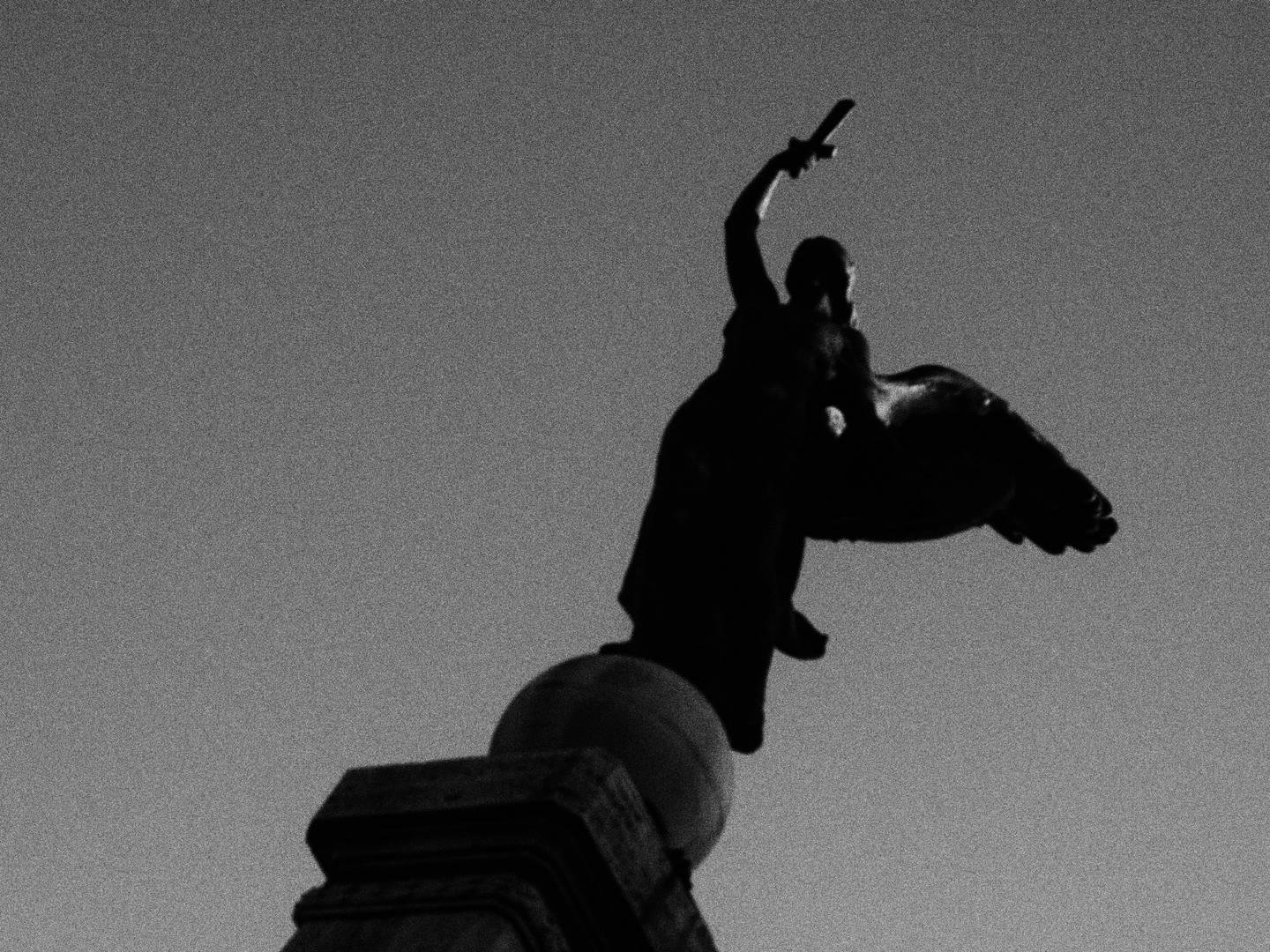 Statua di una donna alata che impugna una corta spada, poggiata su una sfera in cima a un piedistallo.