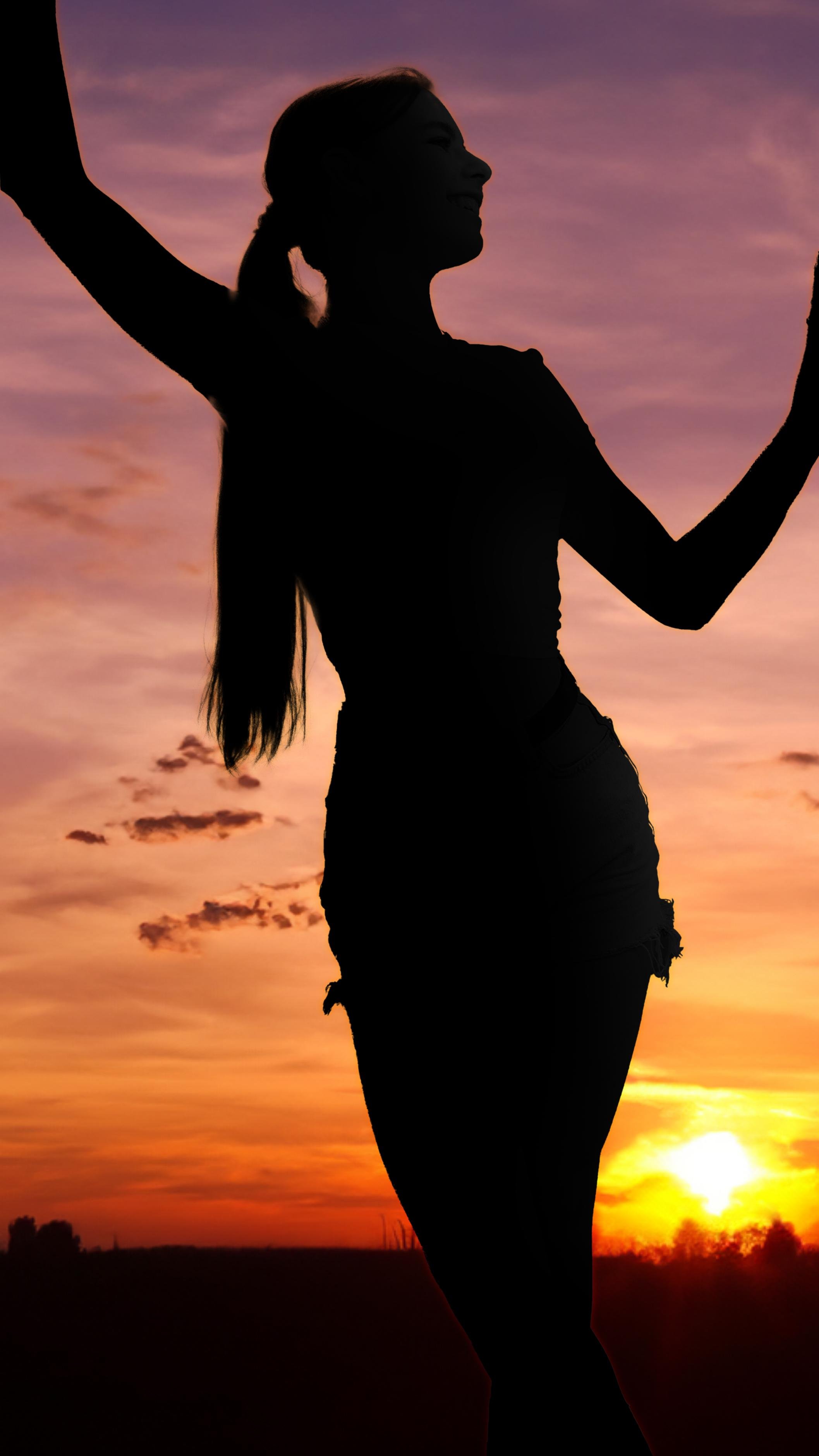 The image shows the silhouette of a person standing against a colorful sunset or sunrise sky. The person appears to have their arms extended and is standing in a natural landscape.