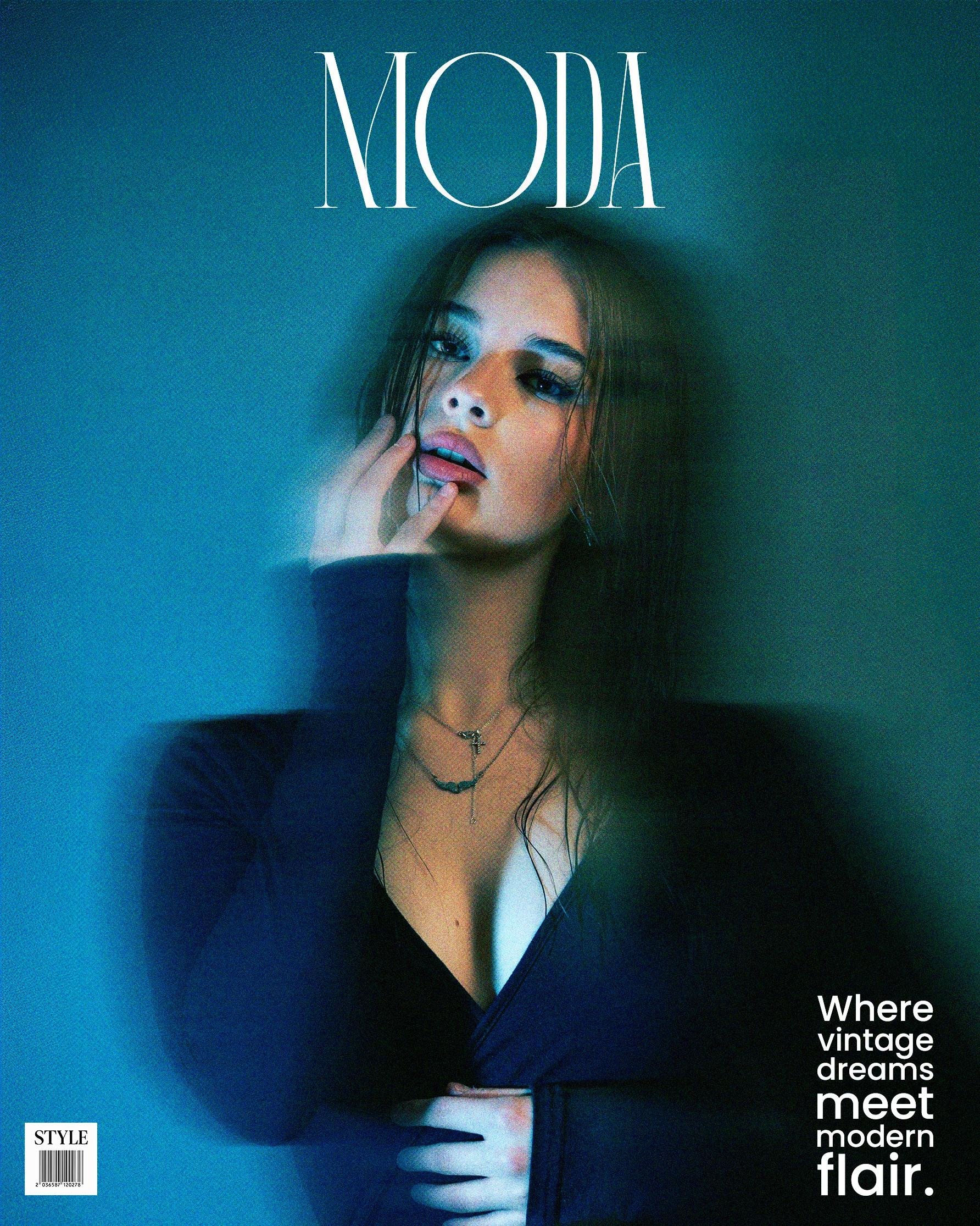 Woman with long hair wearing a dark, low-cut blouse, and layered necklaces. Her left hand is near her face, and she has a soft, blurred expression against a blue, dimly lit background. The word "MODA" is at the top in large text. Bottom right features the phrase "Where vintage dreams meet modern flair" in smaller text. Bottom left shows a small style bar code.