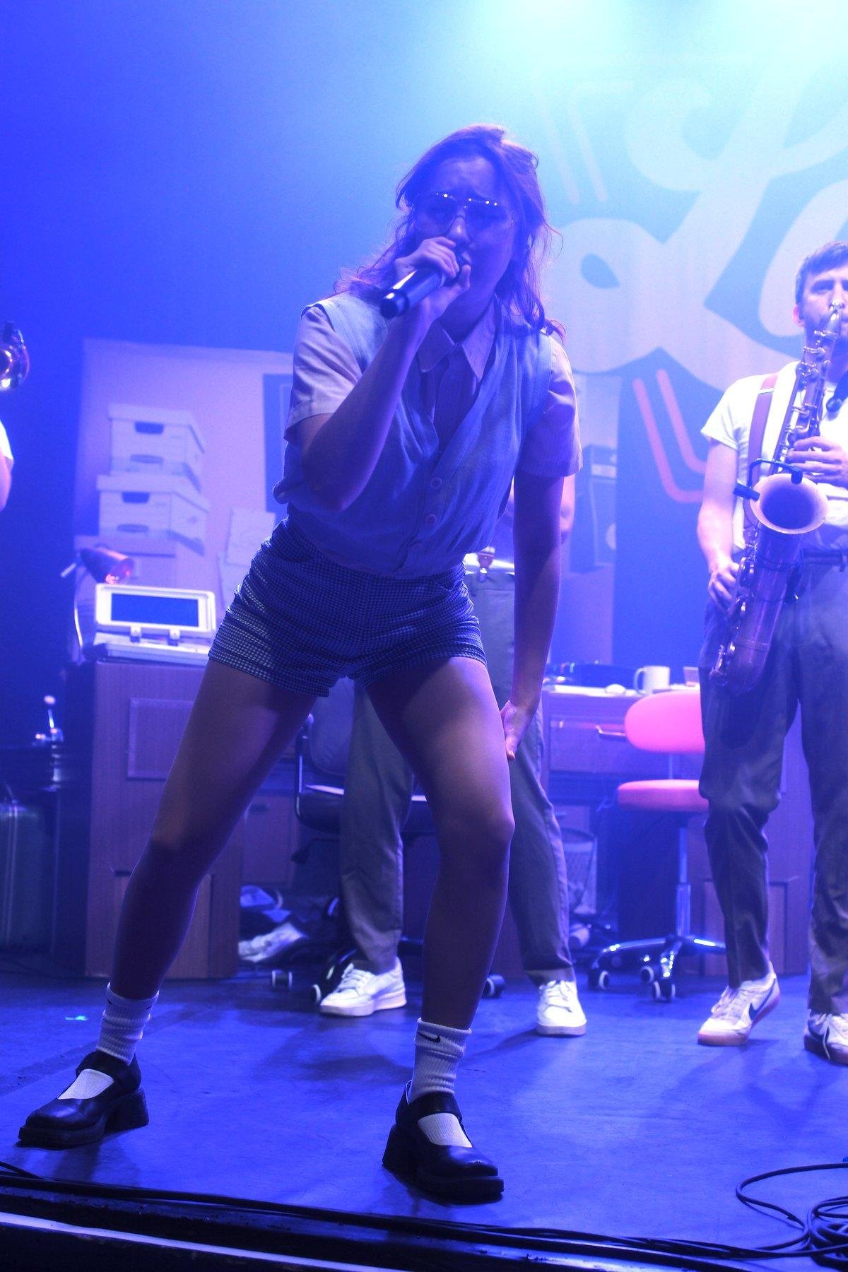 Photo verticale. Gracie Lawrence chantant dans une pose badass, appuyée sur sa jambe gauche