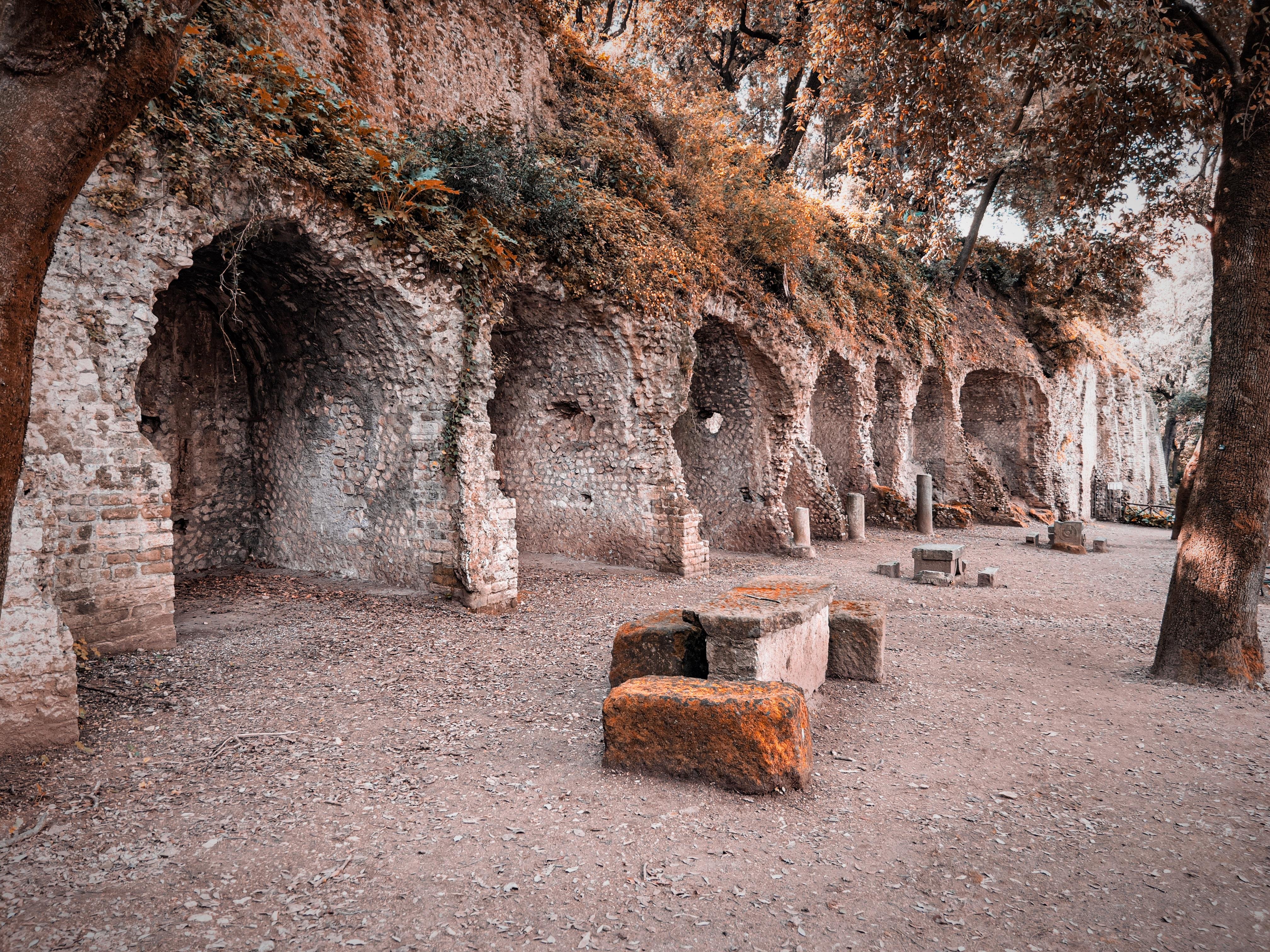 Antichi archi di pietra costruiti su un pendio, probabilmente parte di rovine storiche. L'area è circondata da alberi e sembra essere un sito archeologico all'aperto. Ci sono panche di pietra e resti di vecchie strutture sparsi in giro, conferendo al luogo un'atmosfera storica e serena.