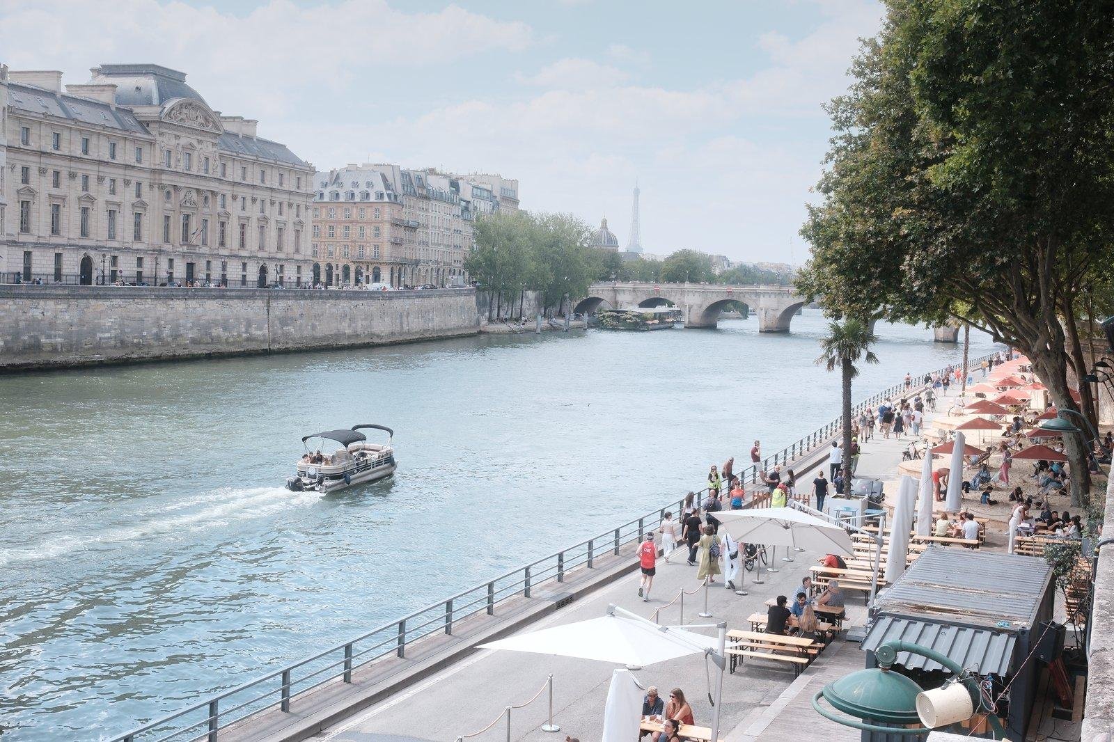 Photo horizontale. La Seine à Paris avec un petit bateau qui remonte l’image, et les quais sur la droite