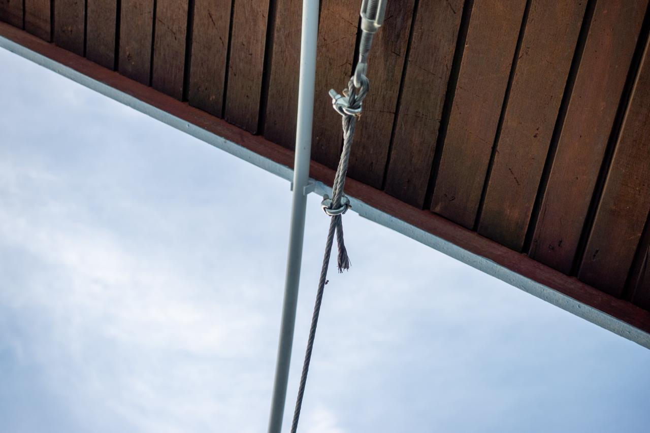 Wooden planks arranged horizontally create a slanted roof-like structure with visible support beams. A metal rope with a hook and cable is attached underneath the structure. The background shows a clear, light blue sky.