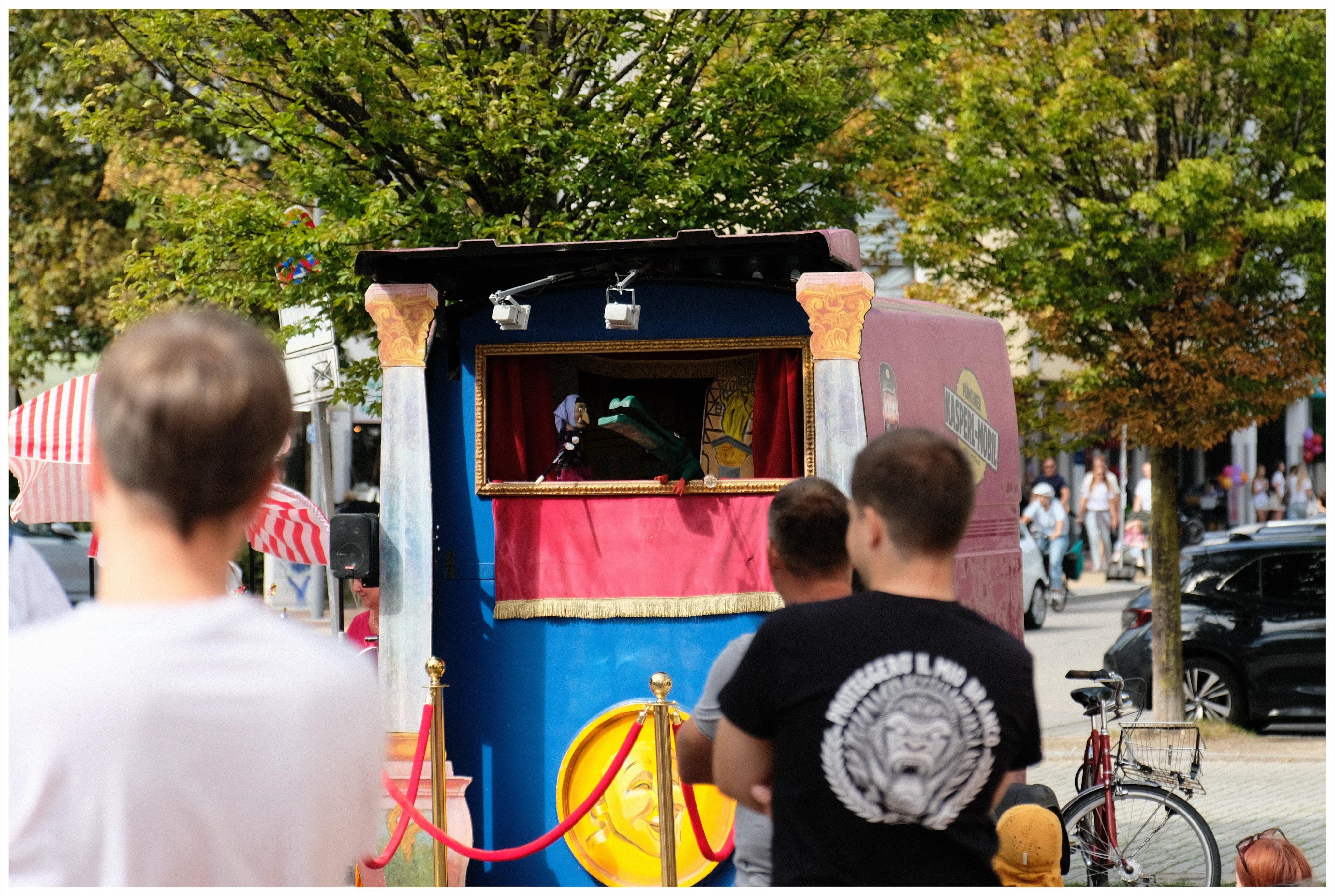 Three men watching a puppet show at a local street festival.