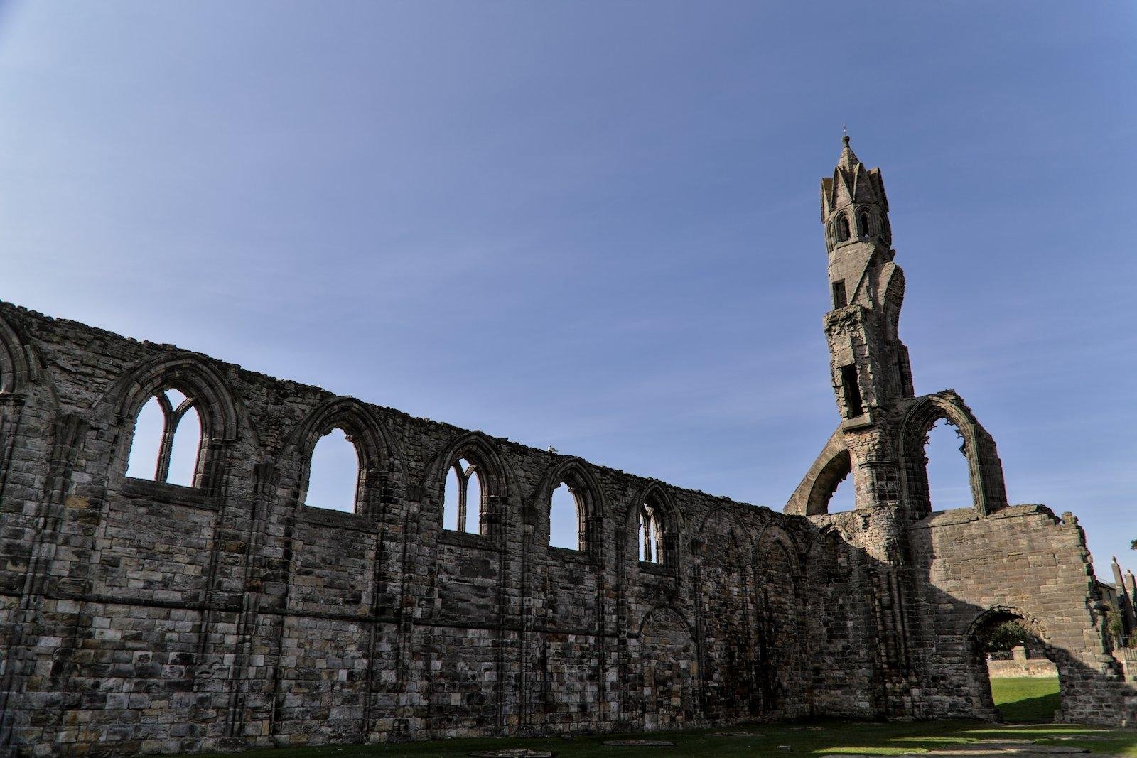 Un des murs des ruines de la cathédrale de St Andrews en Écosse, avec une tour au bout, au fond de la photo, sous un beau ciel bleu
