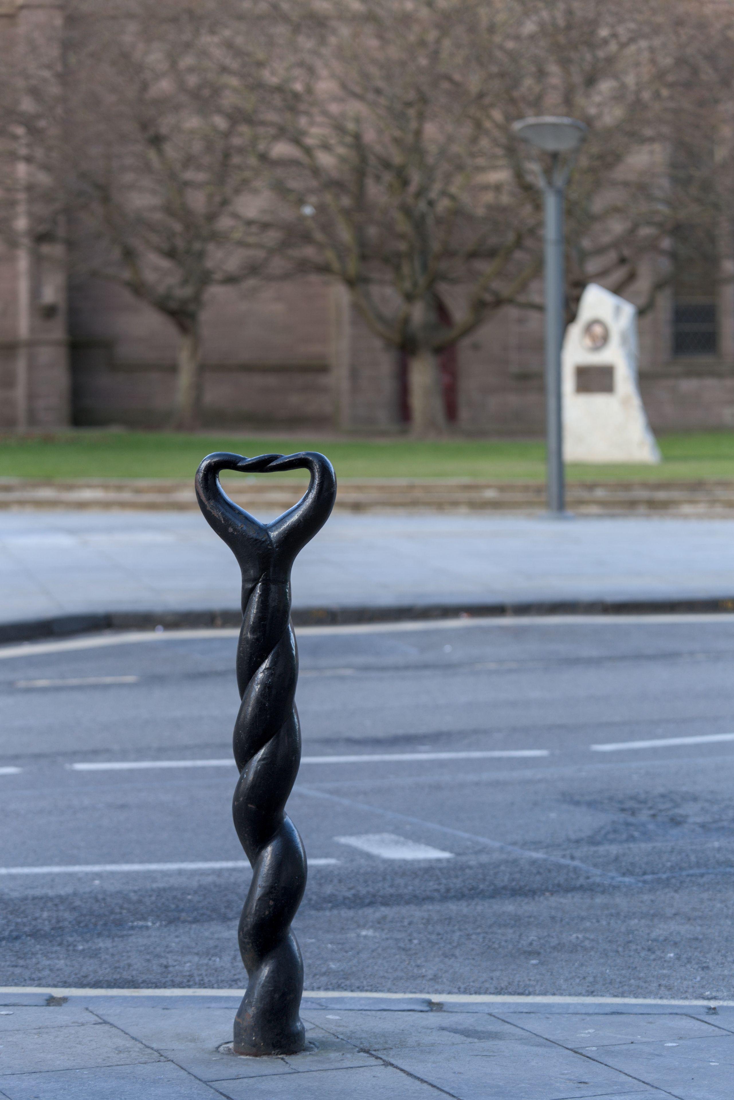 Photo format portrait d’un poteau de rue noir et torsadé dont le sommet peut faire penser à un décapsuleur