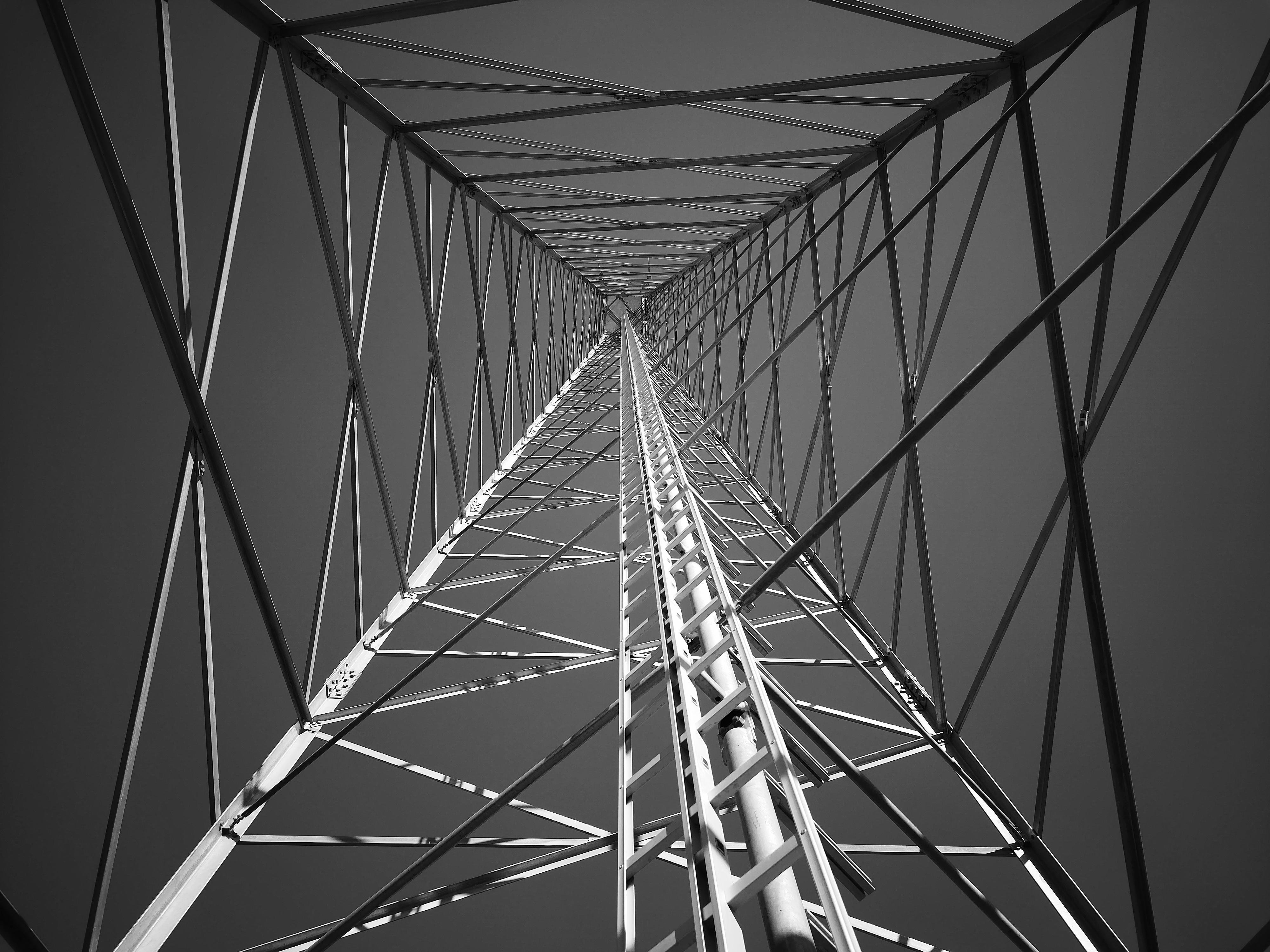 This image shows the inside view of a steel lattice structure, likely a radio or transmission tower. It is shot from below, looking upward, giving a perspective that emphasizes the geometric patterns formed by the intersecting metal beams. The tower's design creates a sense of depth and symmetry.