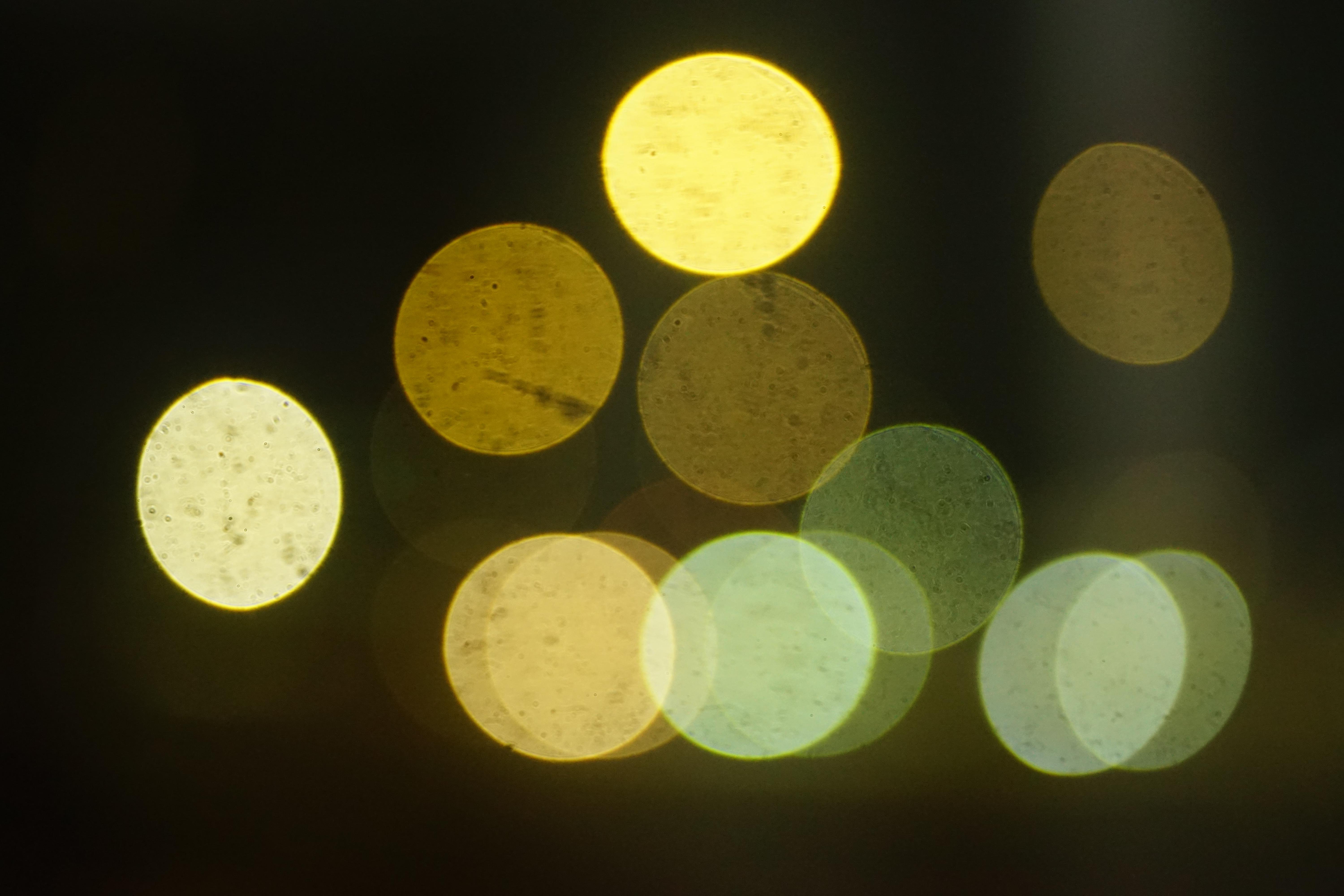 Out-of-focus circular bokeh lights in yellow and pale green on a dark background, clustered near the center with one bright circle at the top and several overlapping circles along the lower edge.