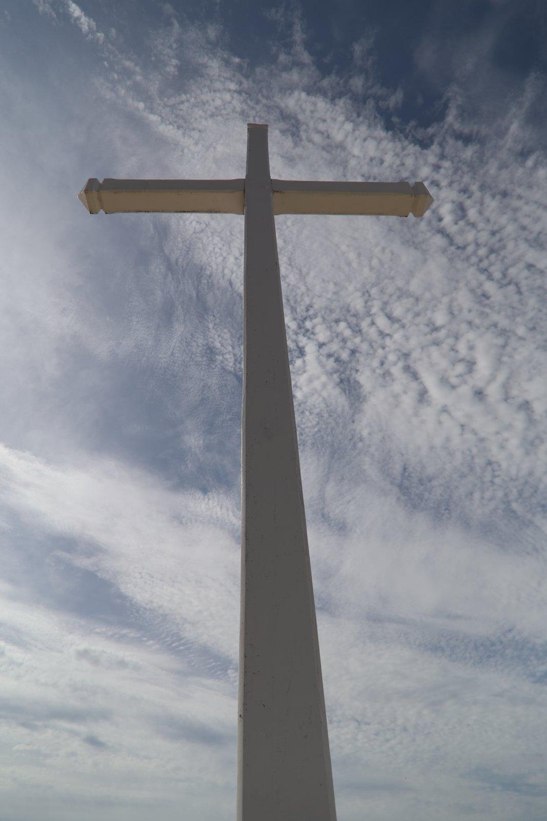Photo format portrait en contre plongée sur une énorme croix blanche sur fond de ciel bleu strié de nuages