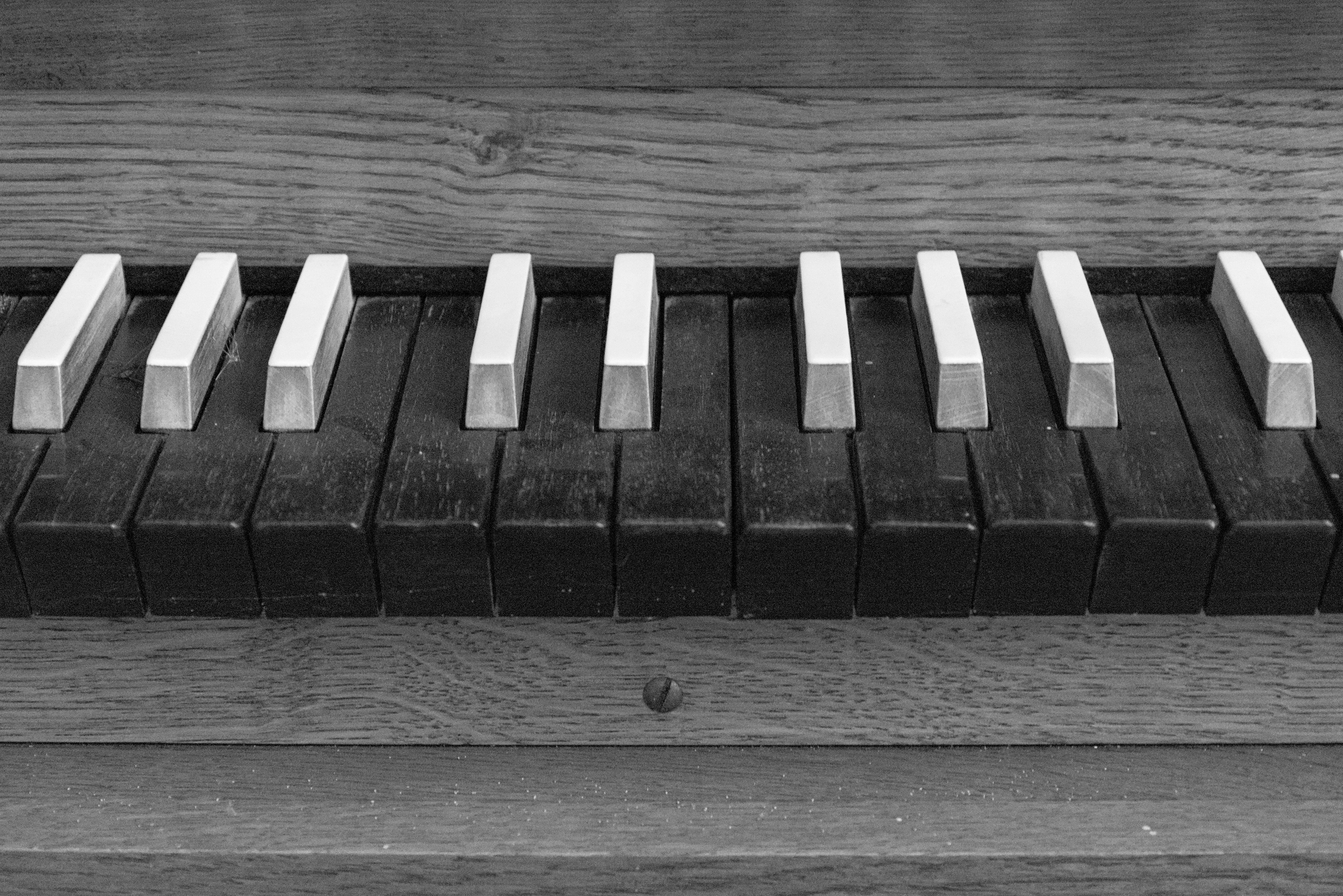 This image shows a close-up of the keys of an old piano or keyboard. The keys appear to have aged, with the white keys looking particularly worn. The overall tone is black and white, giving it a vintage appearance.