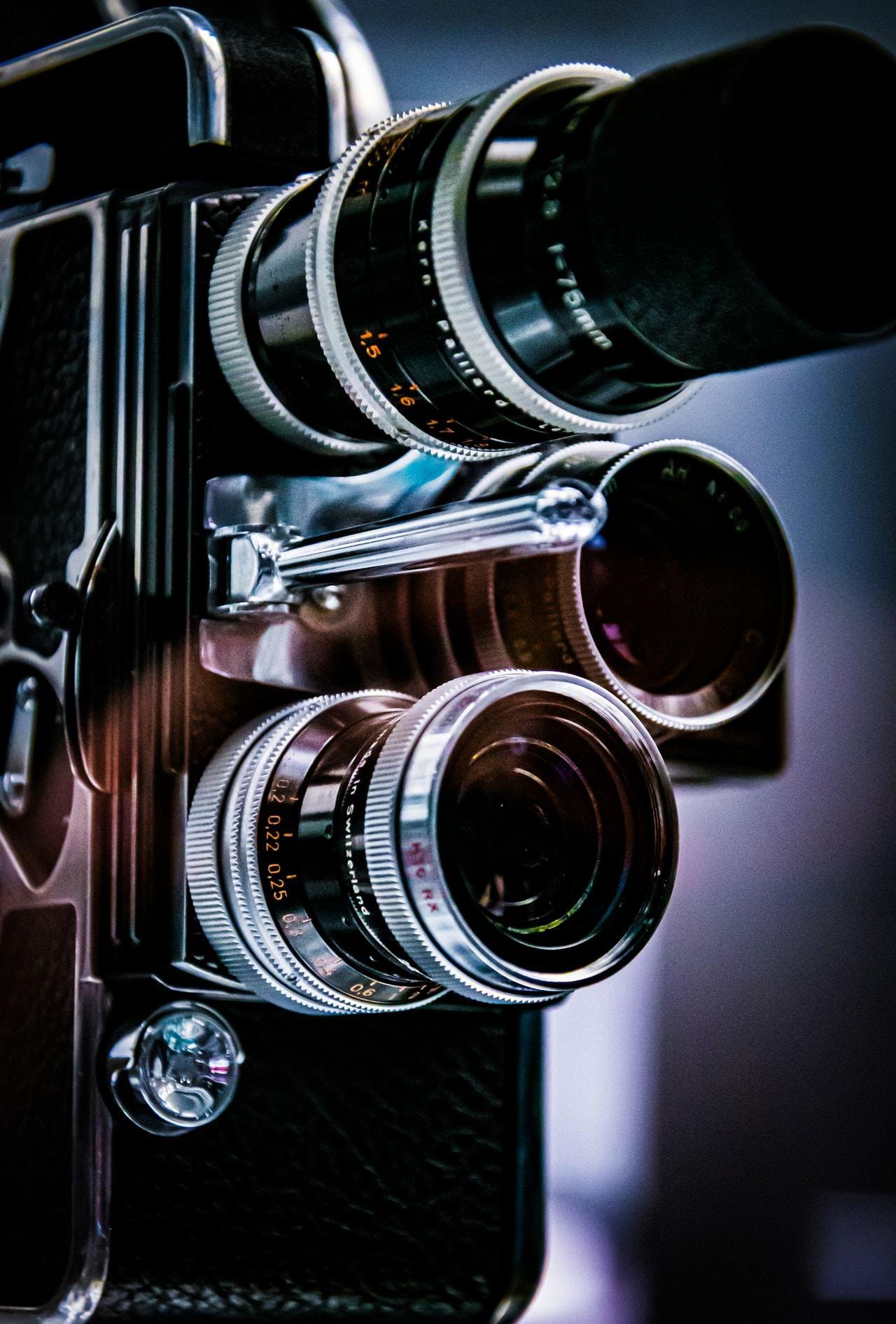 Close-up of a vintage twin-lens reflex camera, showing two stacked circular lenses with silver focus rings and a black body against a blurred dark background.