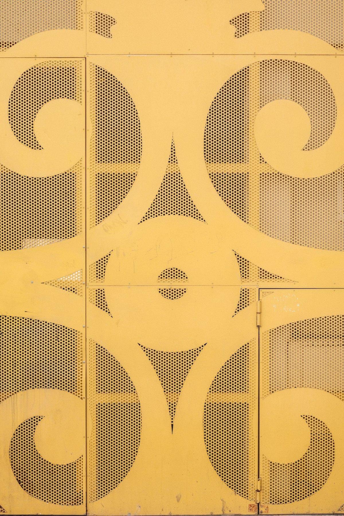 Photo verticale. Une porte taillée dans du métal maillé avec des parties pleines formant 4 motifs en spirales symétriques
