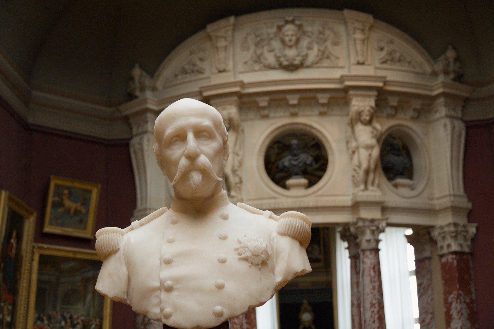 Le buste (en marbre blanc ?) d’un homme avec une belle moustache et un bouc en pierre blanche avec des épaulettes militaires et un écusson sur la poitrine.