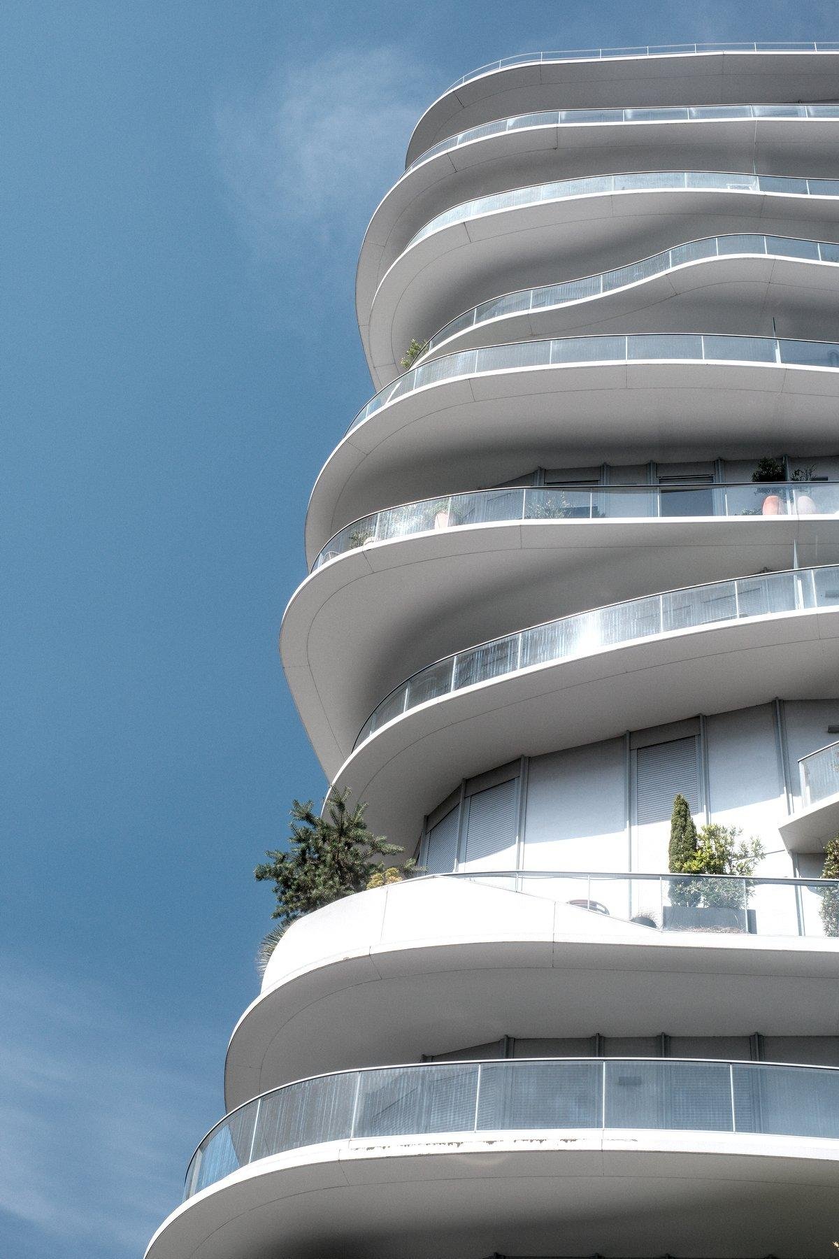 Photo verticale. Des balcon avec une rambarde en verre, en forme de V arrondi mais les étages ne sont pas identiques, comme si on les avait posés un peu à la va vite