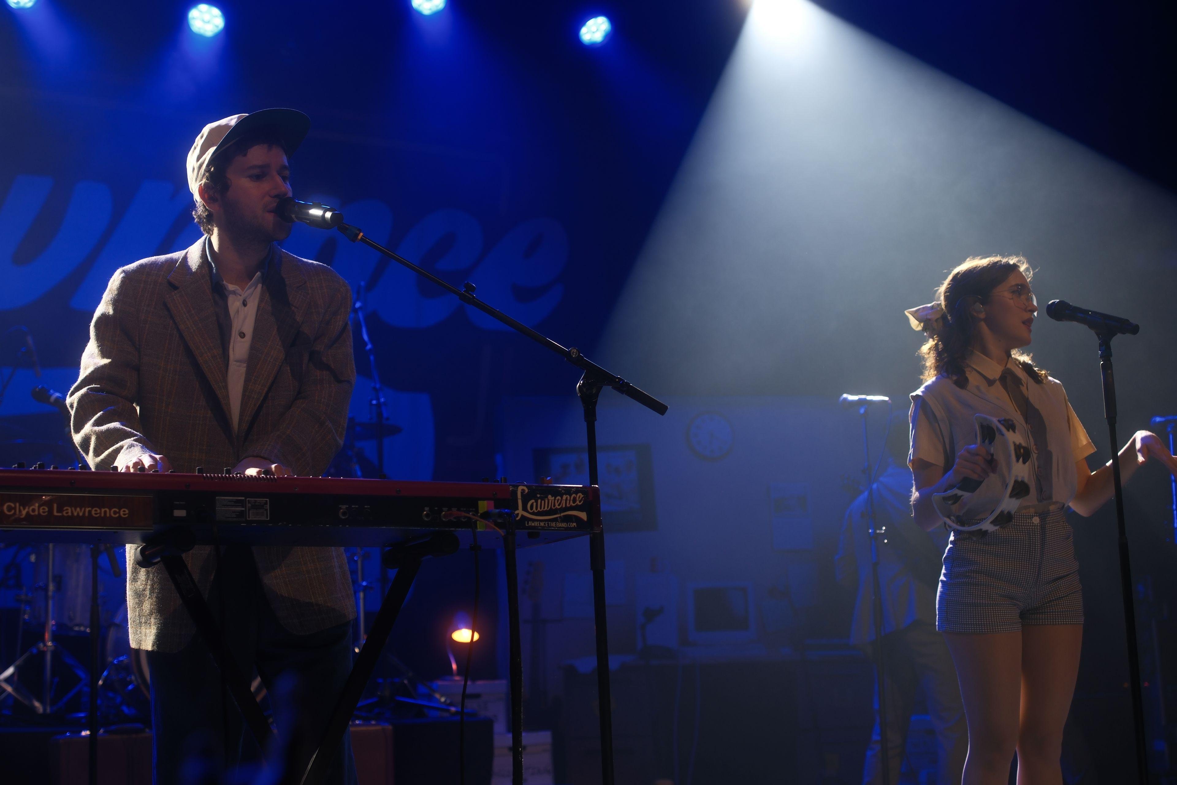 Photo horizontale. Clyde et Gracie Lawrence sur scène, le premier au clavier et la seconde au chant avec un tambourin