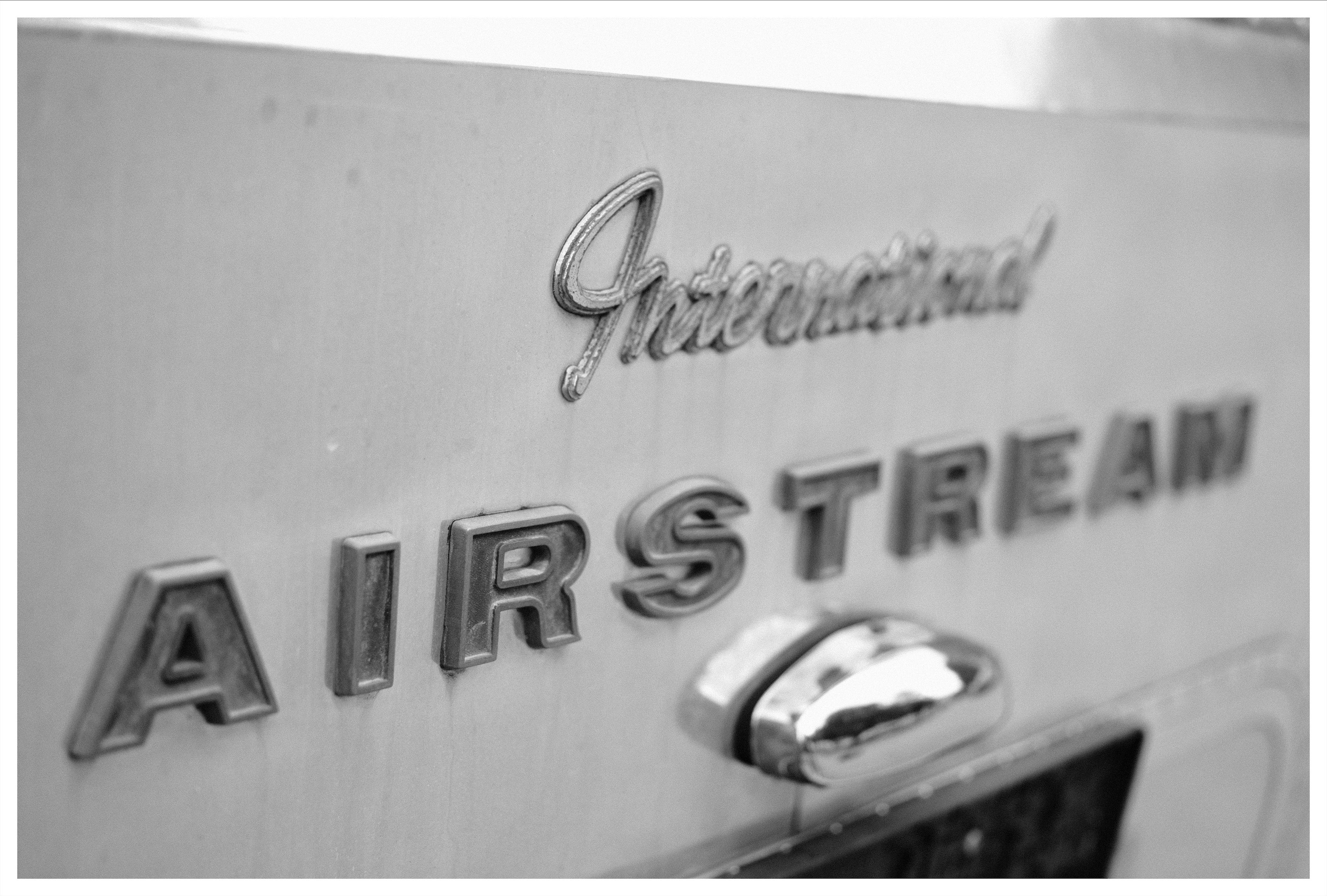 Close-up of a metallic trailer surface with the cursive “International” emblem above raised block letters spelling “AIRSTREAM,” and a chrome handle below, in black and white.