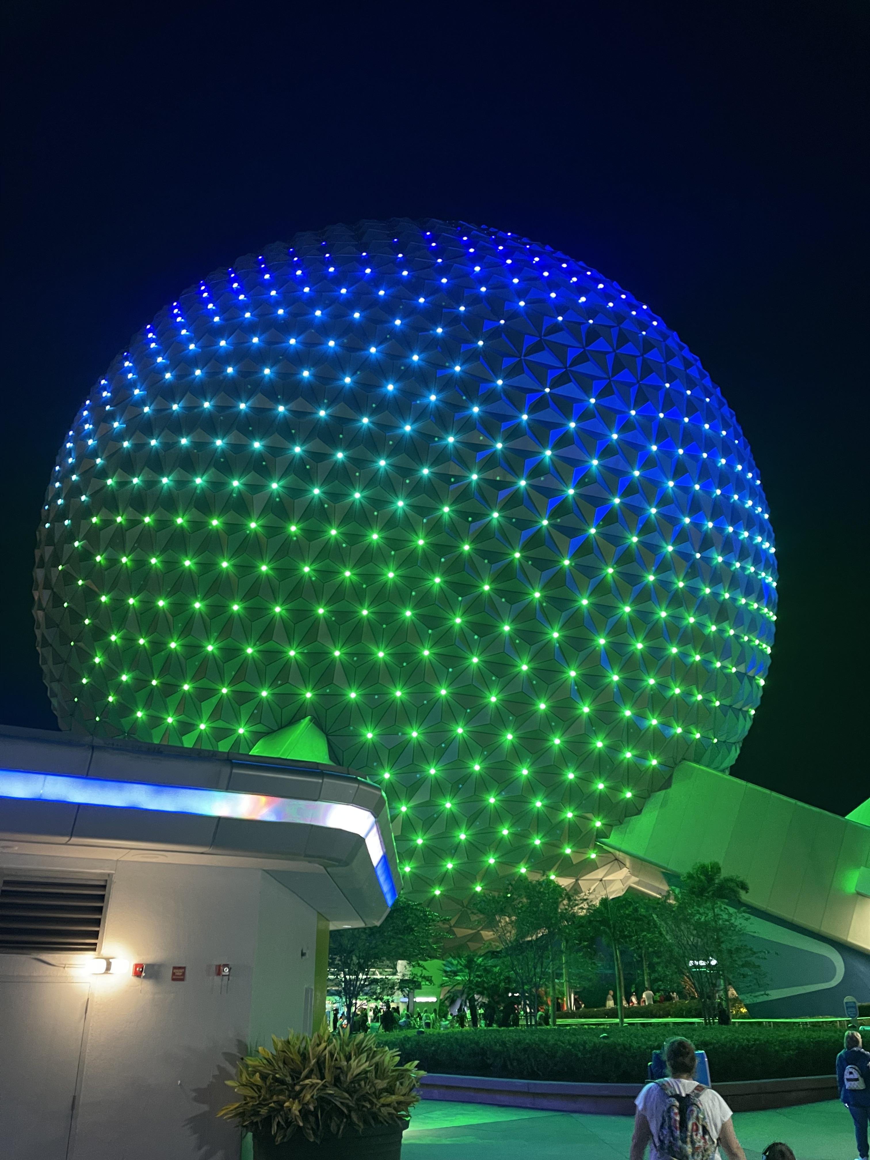 The image shows Spaceship Earth at Epcot, part of the Walt Disney World Resort. It’s a large geodesic sphere that is illuminated with blue and green lights. The structure is an iconic symbol of Epcot and serves as an attraction as well.