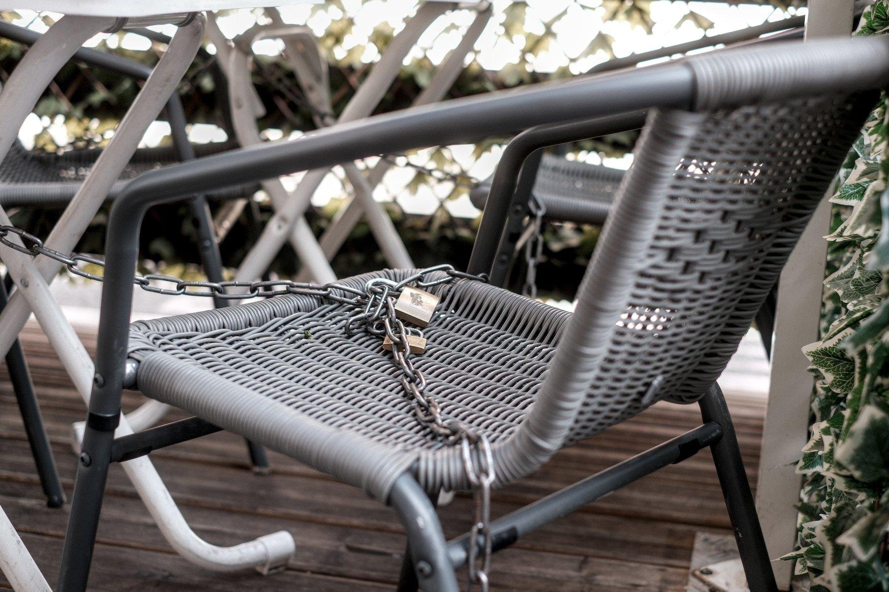 Photo horizontale. Gros plan d’une chaise de jardin sur une terrasse, enchaînée avec des cadenas pour empêcher le vol du mobilier