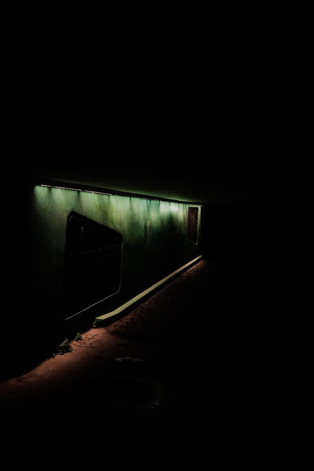 Photo format portrait en couleur, de nuit, on y voit un mur vert avec une grille presque carré, le bord haut descendant de gauche à droite, éclairé par des LED blafardes