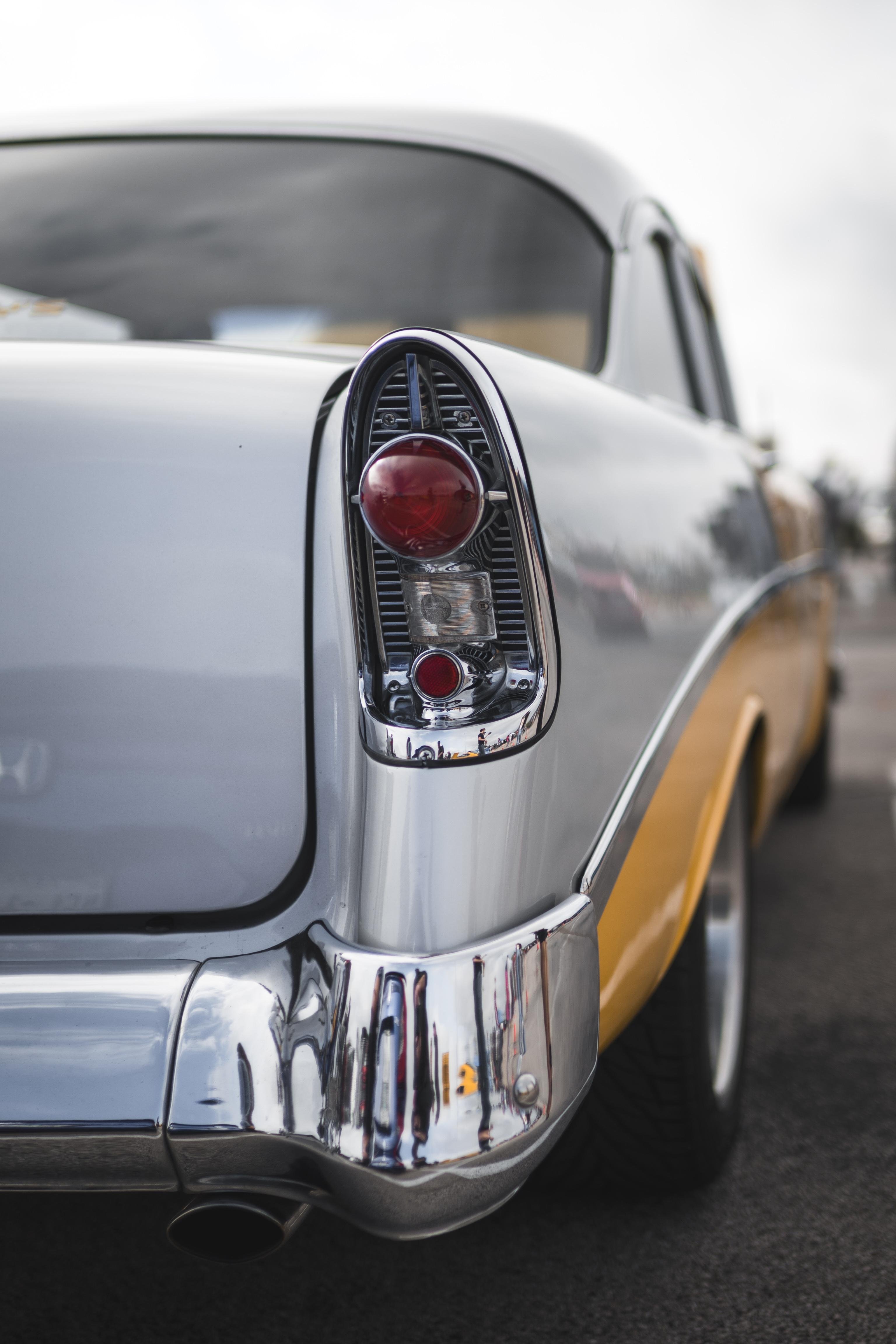 The image shows the rear end of a vintage car, likely from the 1950s. The focus is on the tail light, which is a classic bullet-shaped design. The car is two-toned, with silver and yellow colors, and it features chrome detailing on the bumper.