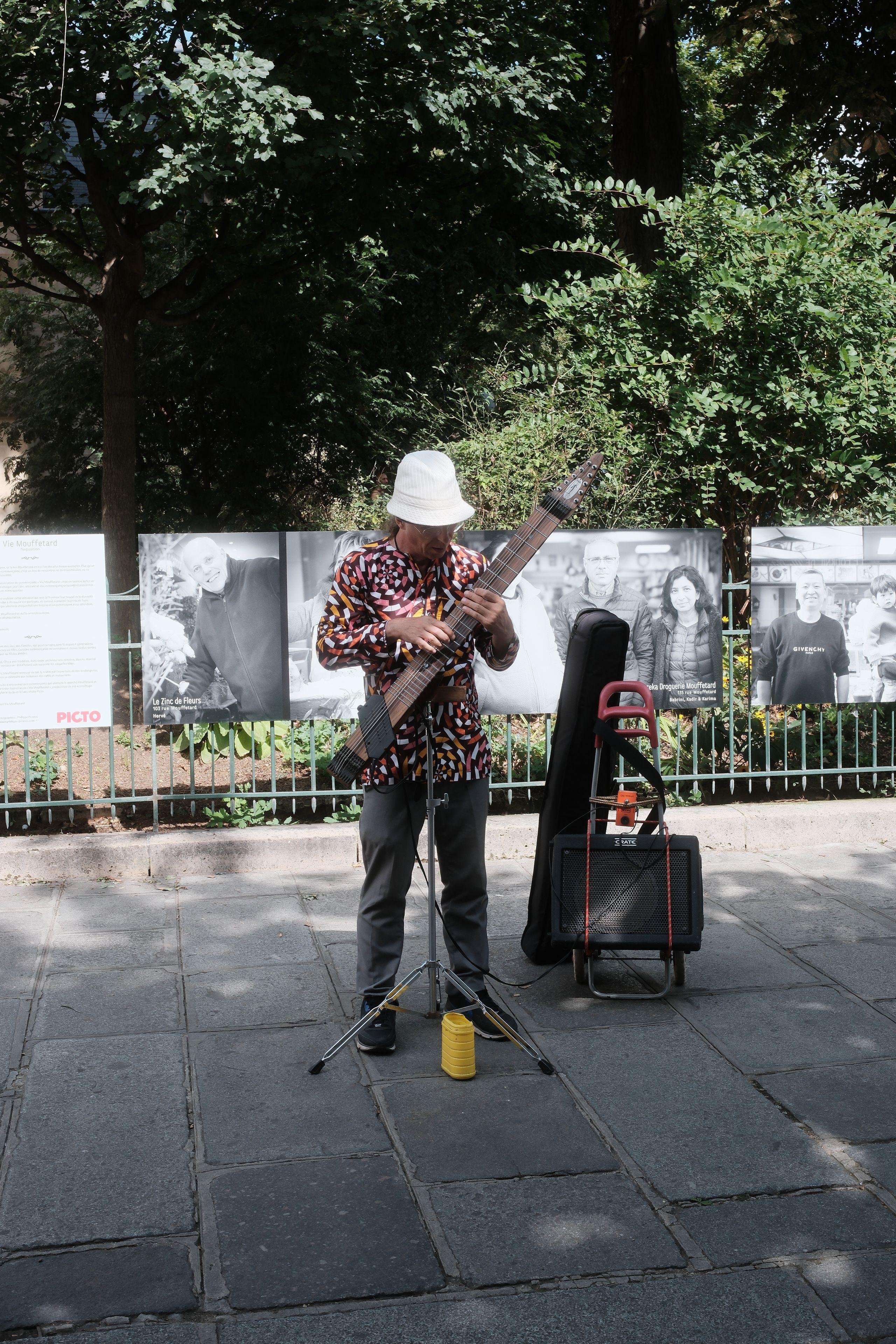 A man busking on the street on an string instrument made of a single block of wood, with a pickup, linked to an amp (a Chapman stick)