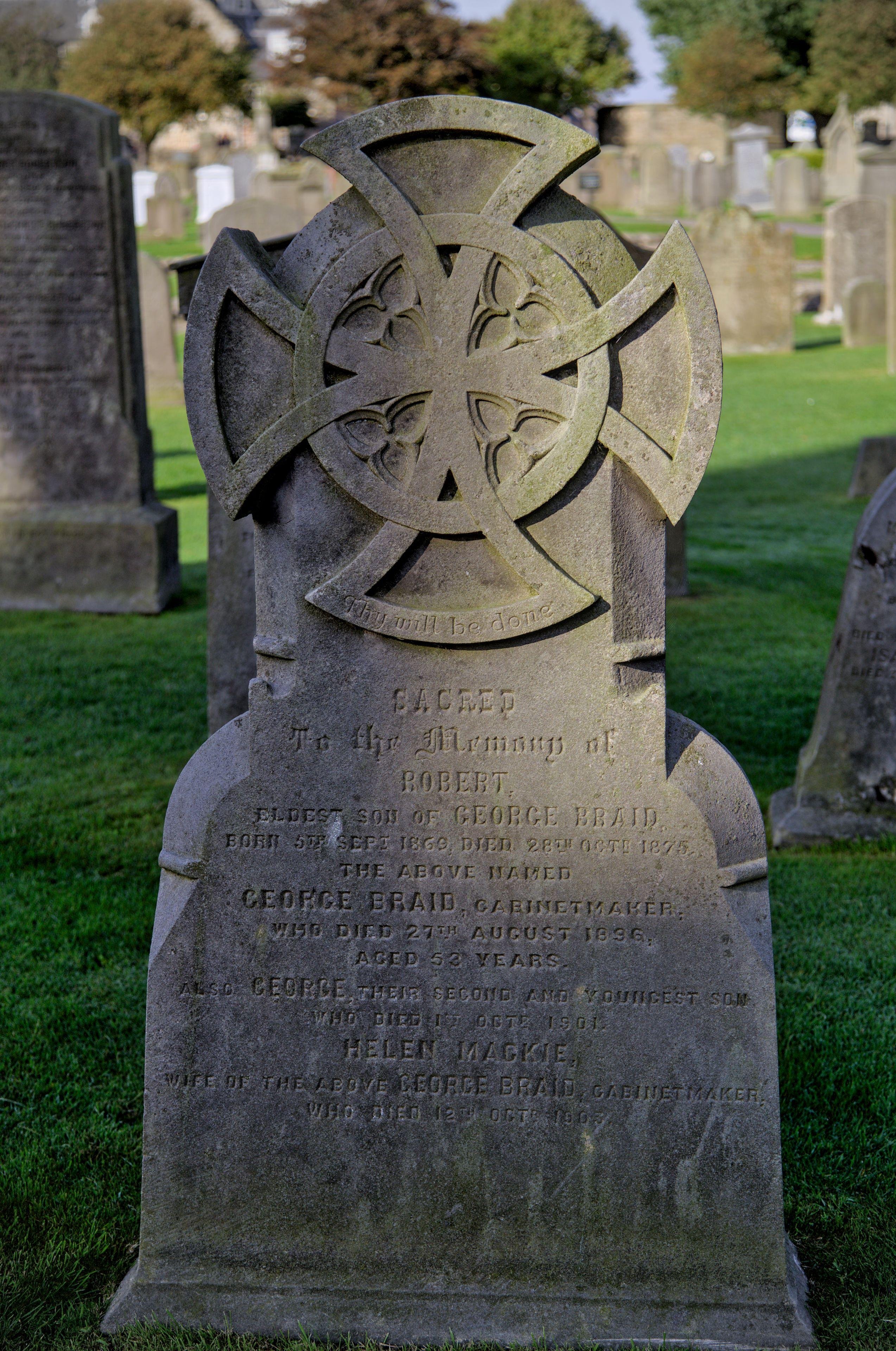 Une pierre tombale ancienne avec une croix aux 4 branches identiques, reliées par un cercle. D’autre tombes sont visibles en fond