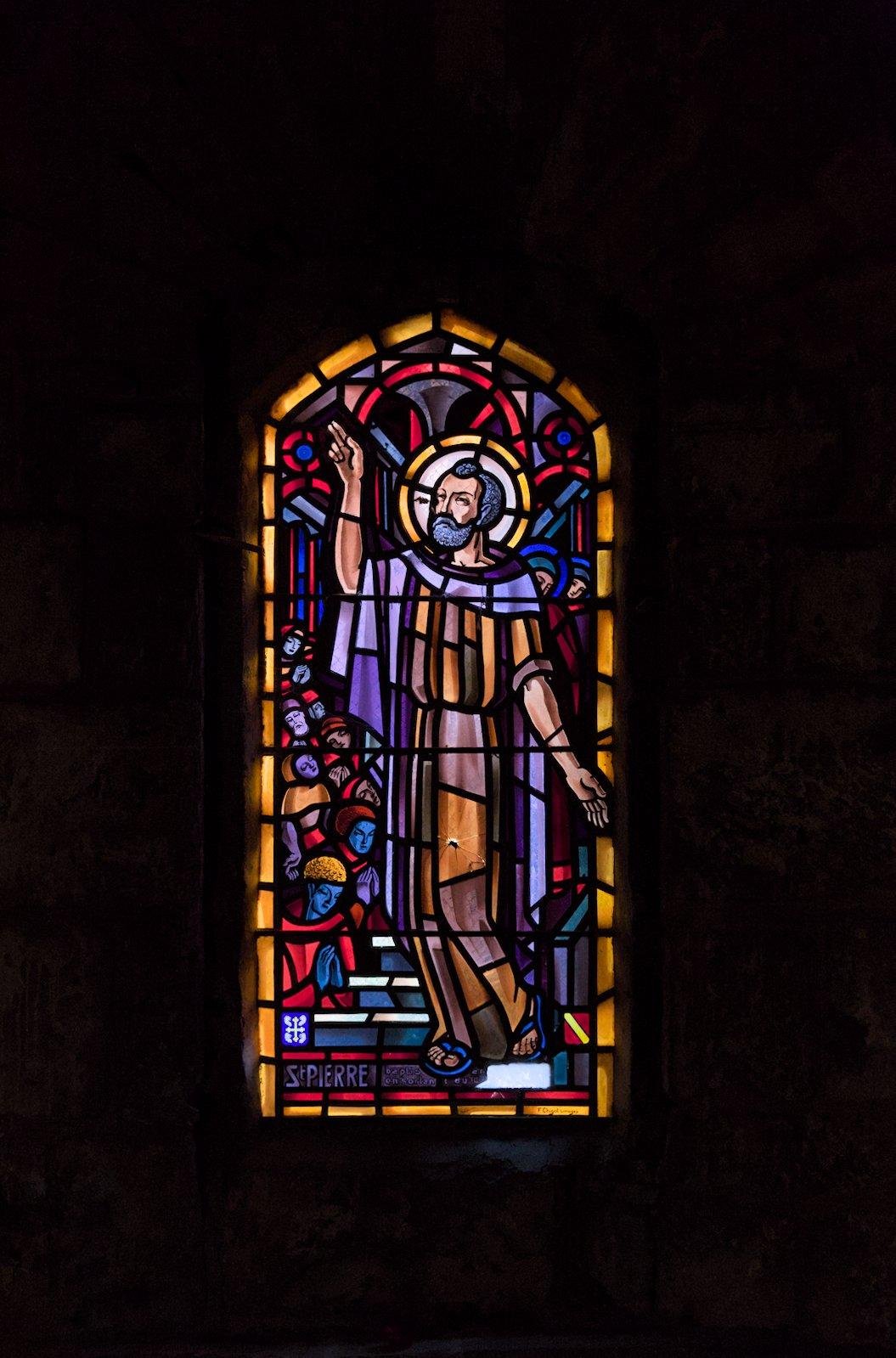 Photo format portrait d’un vitrail représentant St Pierre, un impacte est visible au niveau du genoux