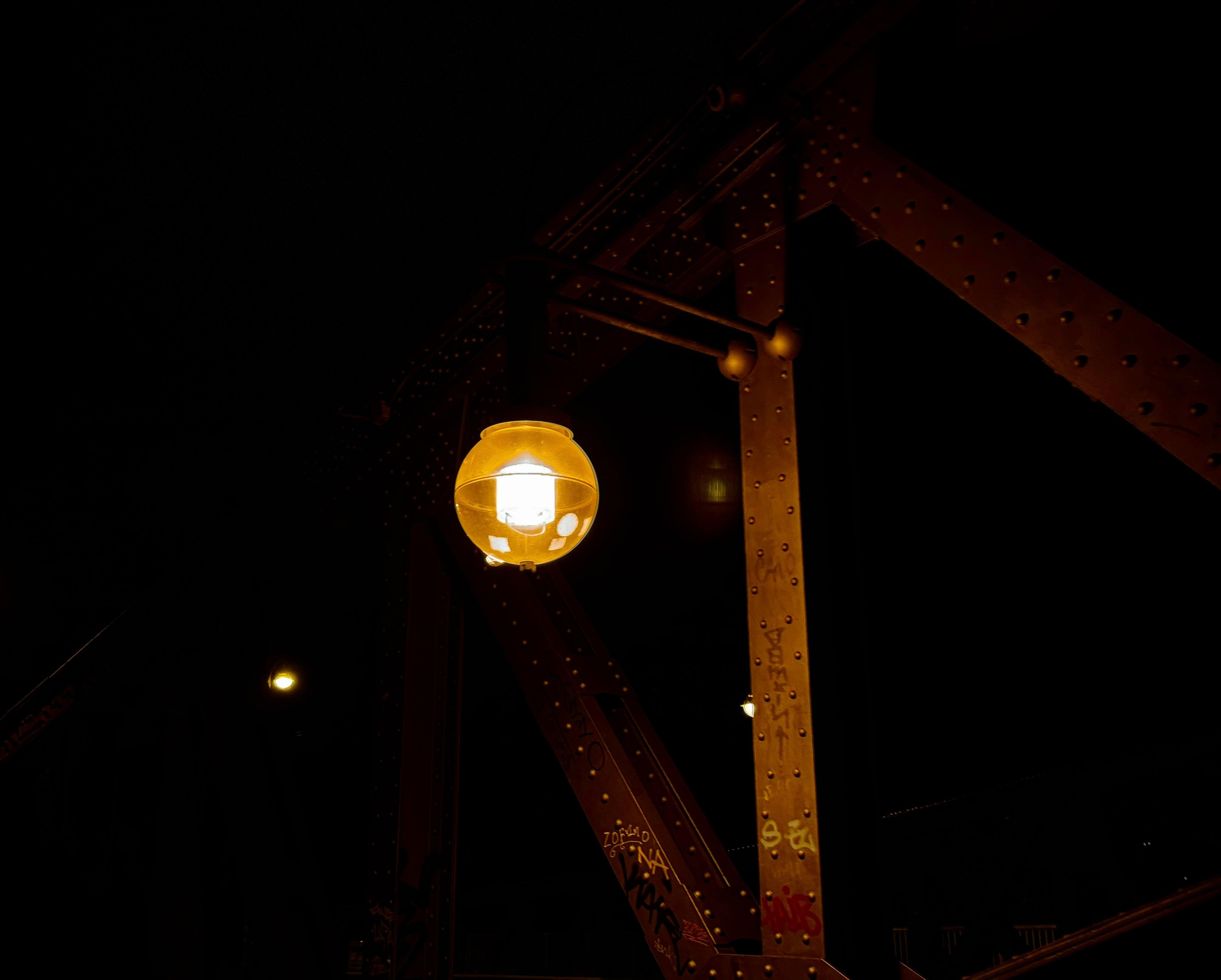 A glowing yellow light fixture attached to a metal structure under a dark sky.