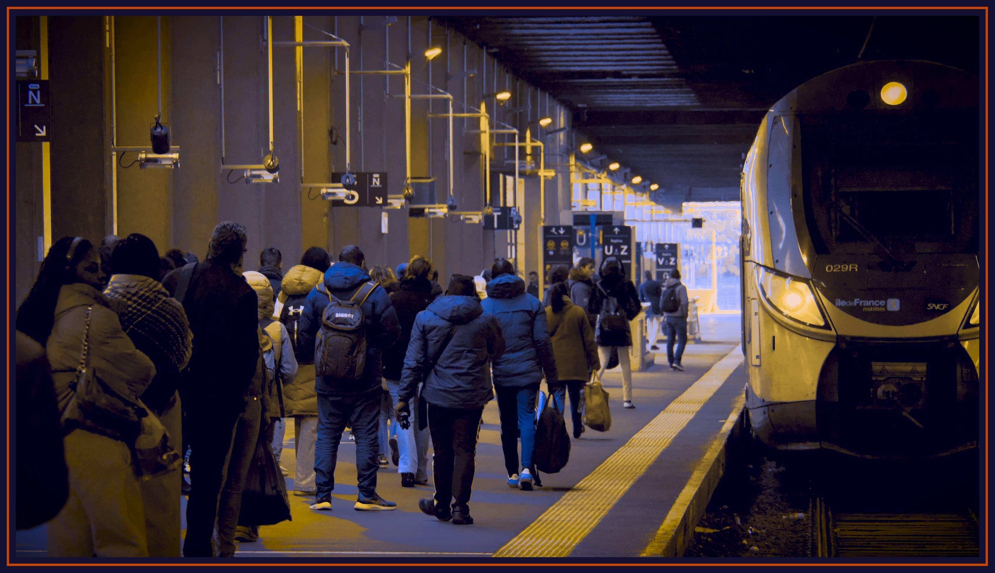 Les deux photographies représentent un quai de gare avec des personnes marchant le long du quai. Un train est sur les rails à côté d'eux. Des panneaux et des lumières sont visibles au-dessus des personnes, indiquant les numéros de quai. Elles sont encadrées par un pourtour bleu foncé et un liseré orange. Cette version de la photo propose un contraste de couleurs élevé entre l'orange et le bleu, donnant une ambiance à la fois de fin de journée, mais aussi une sensation que toutes les bonnes choses ont une fin.