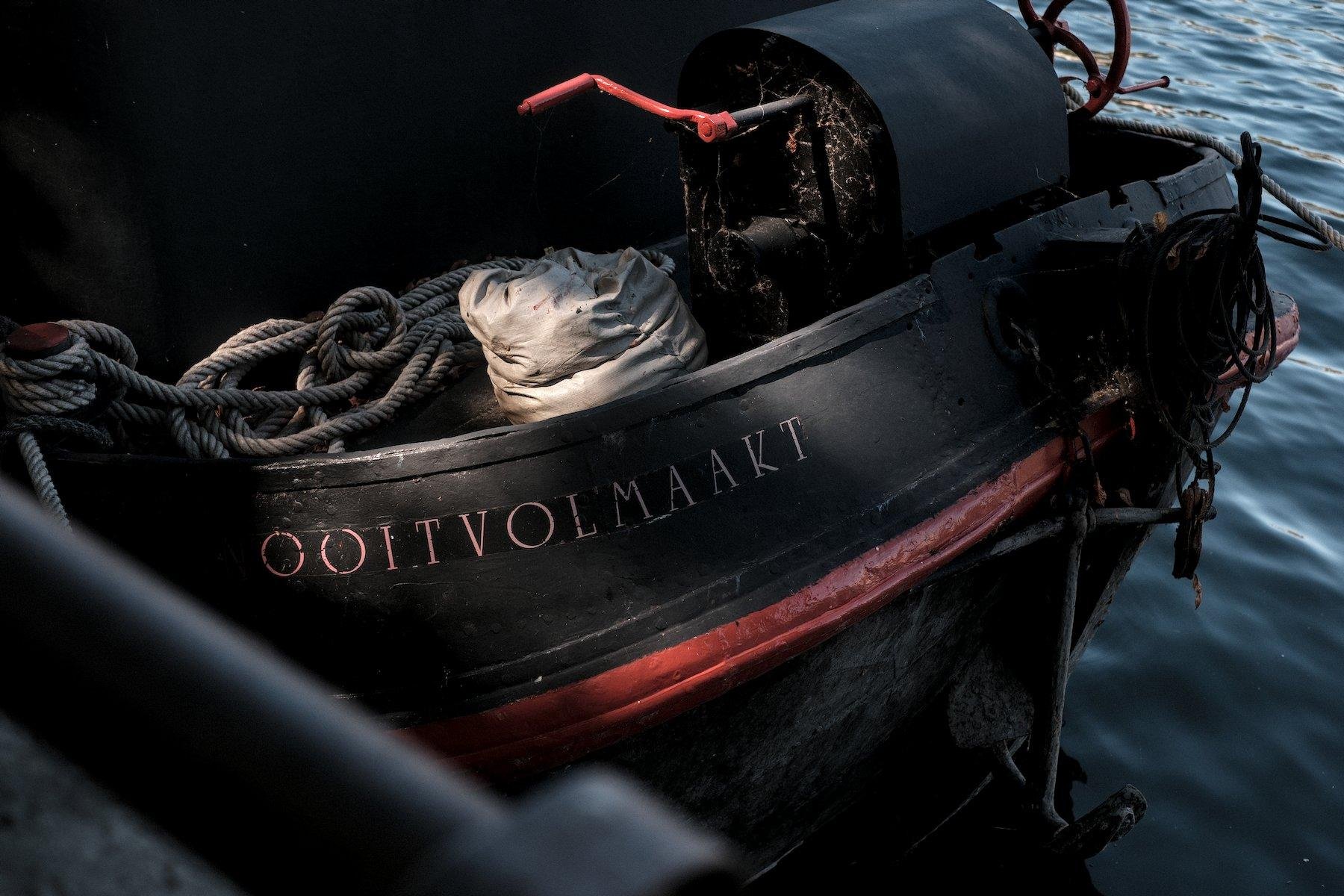 Photo horizontale. La proue d’un bateau, noire, avec des accents rouge, avec son nom en lettres capitales « OOLTVOLMAAKT »