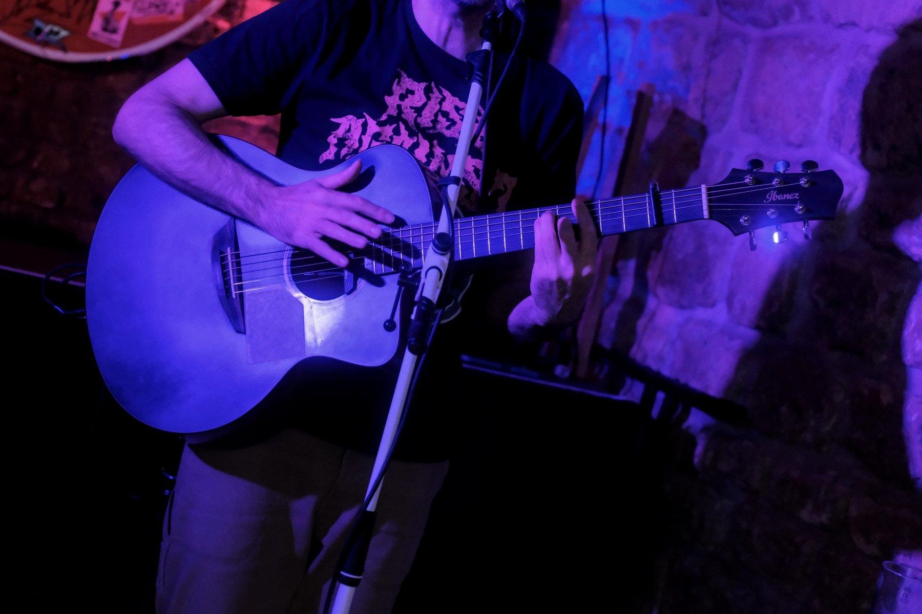 Photo horizontale. Une guitare acoustique noire entrain d’être jouée comme une percussion