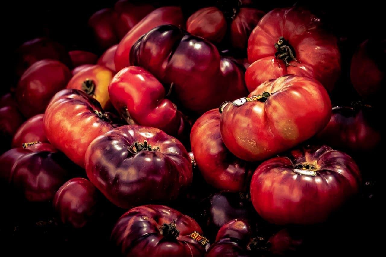 The image shows a pile of heirloom tomatoes. They have a variety of shapes and a mix of red, purple, and orange colors.