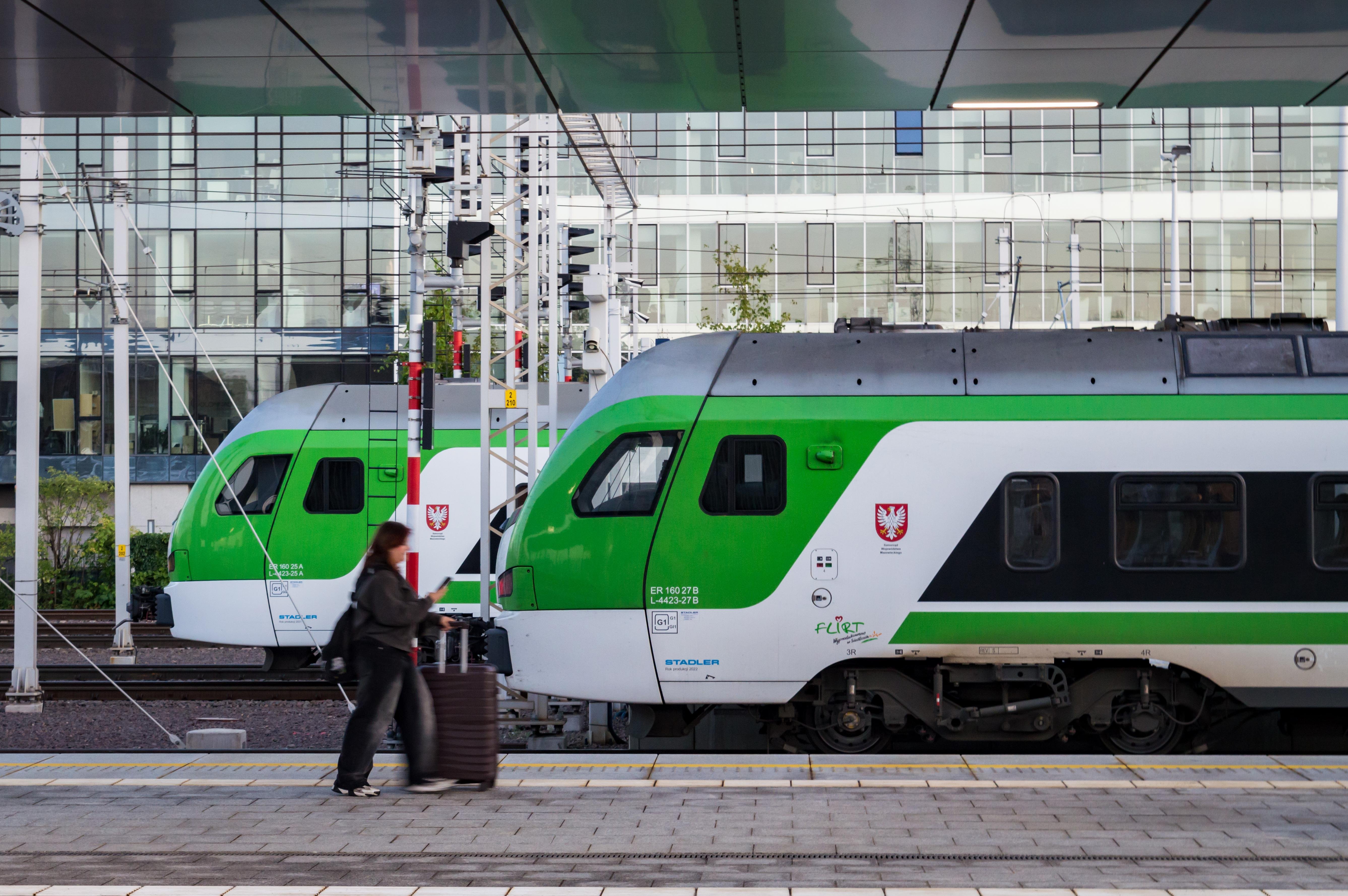 Person with suitcase walking on a platform of Warsaw West in front of two Stadler Flirt3 EMUs of KM side-by-side