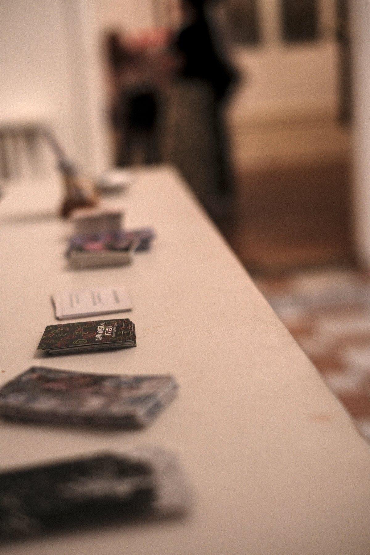 Photo verticale. Sur un comptoir blanc, des cartes de visites, rangées en petit tas par artistes. Seule une est nette, le reste baignant dans le bokeh