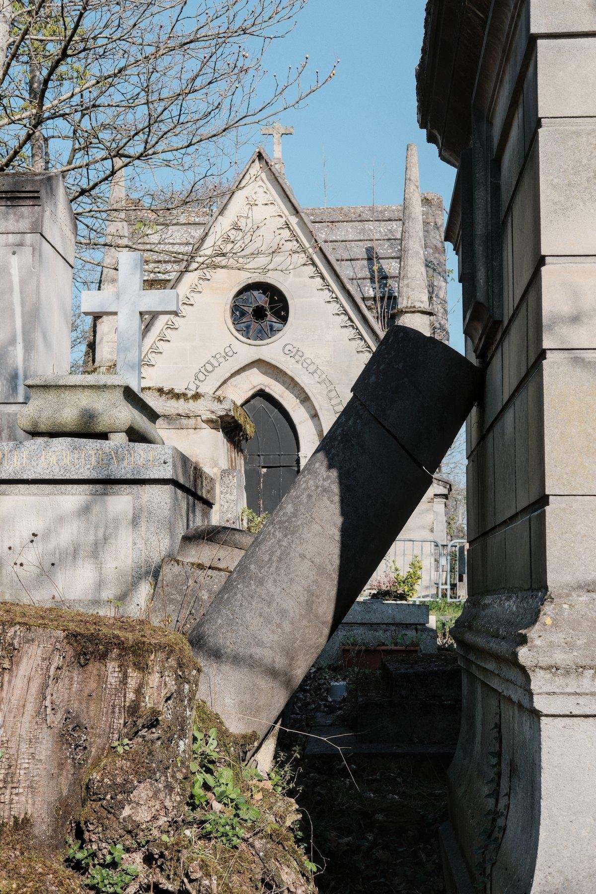 Photo verticale. Une colonne de pierre tombe sur le mur d’un mausolée à droite