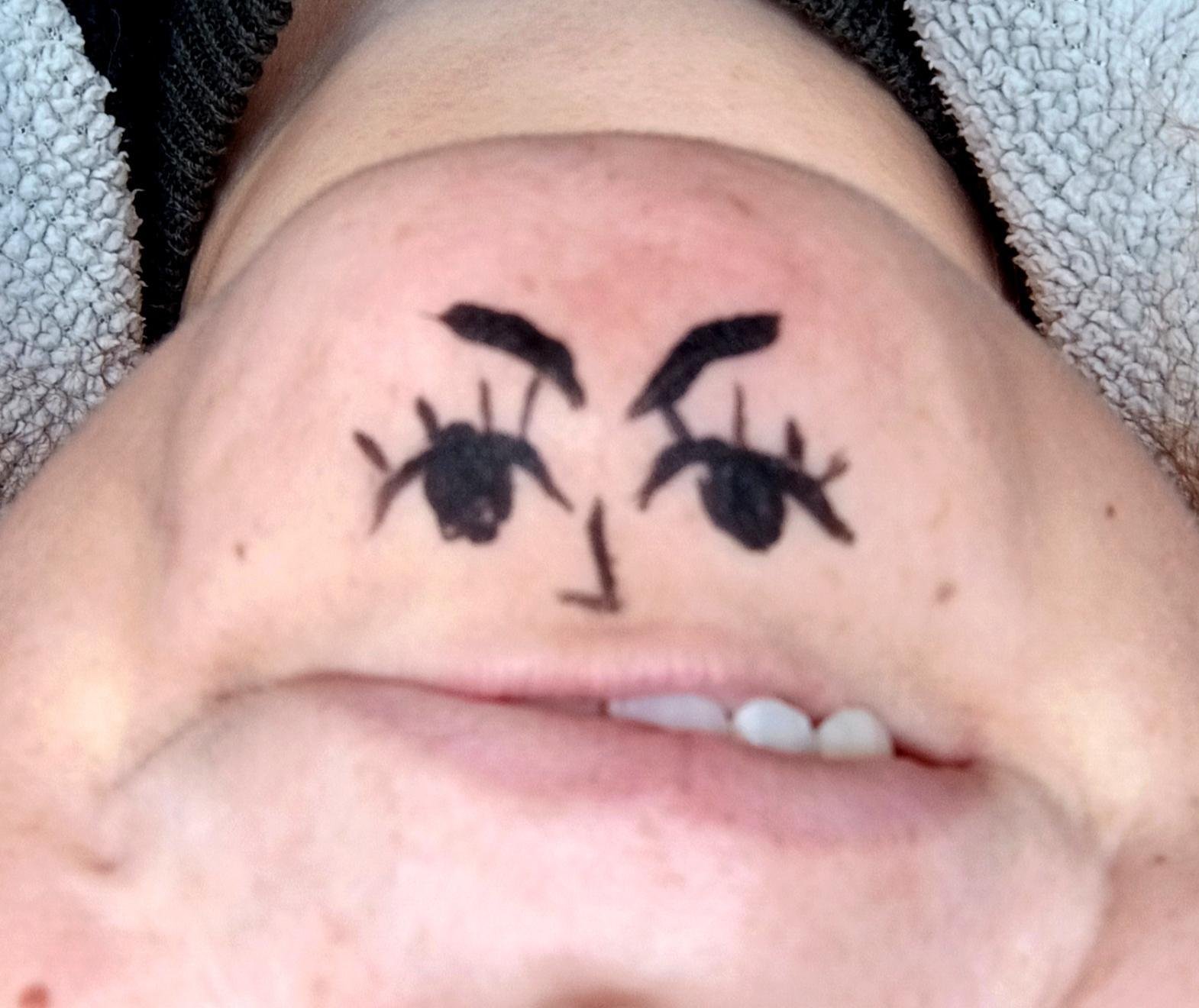 Una foto al revés de una barbilla a la que le han pintado unos ojos y una nariz con eye liner. La boca enseña parte de los dientes. Parece que la barbilla en sí es una cara medio enfadada con dientes
