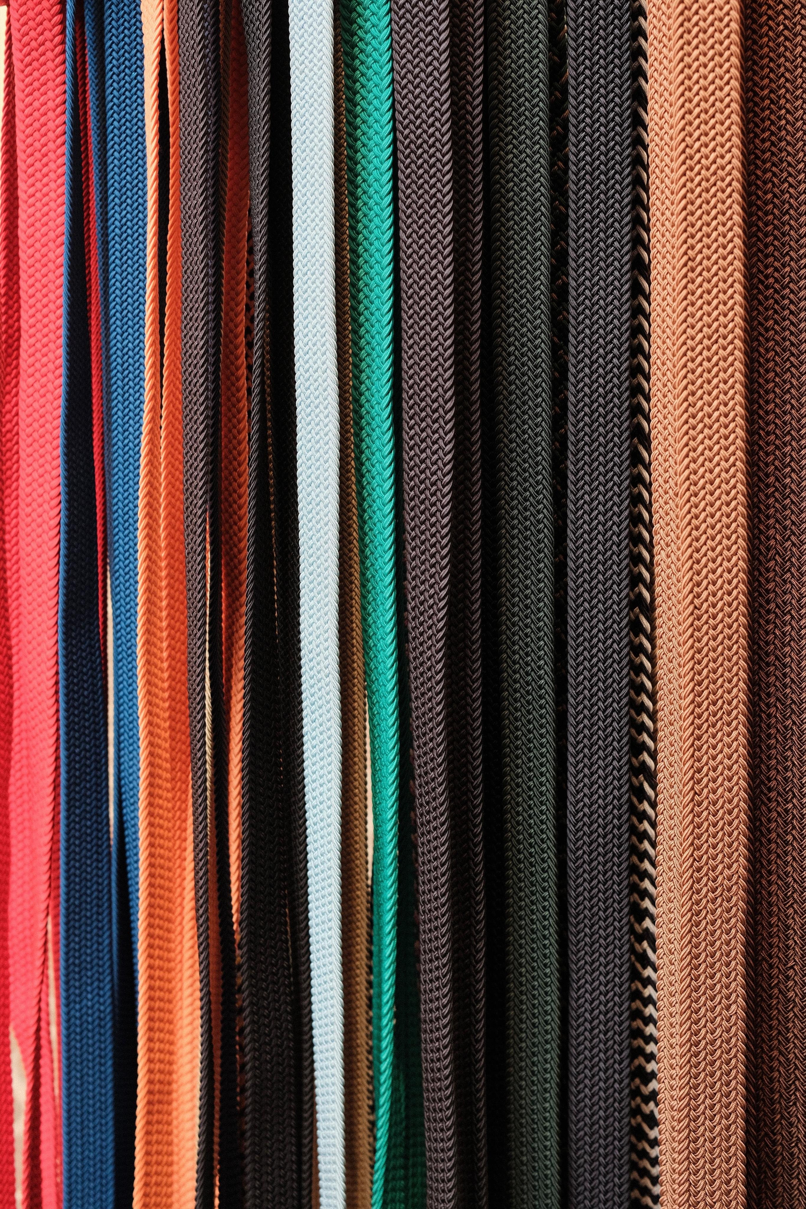 A bunch of colourful woven belts hanging from a shelf in a shop. The woven parts of the densely packed belts fill the whole frame.