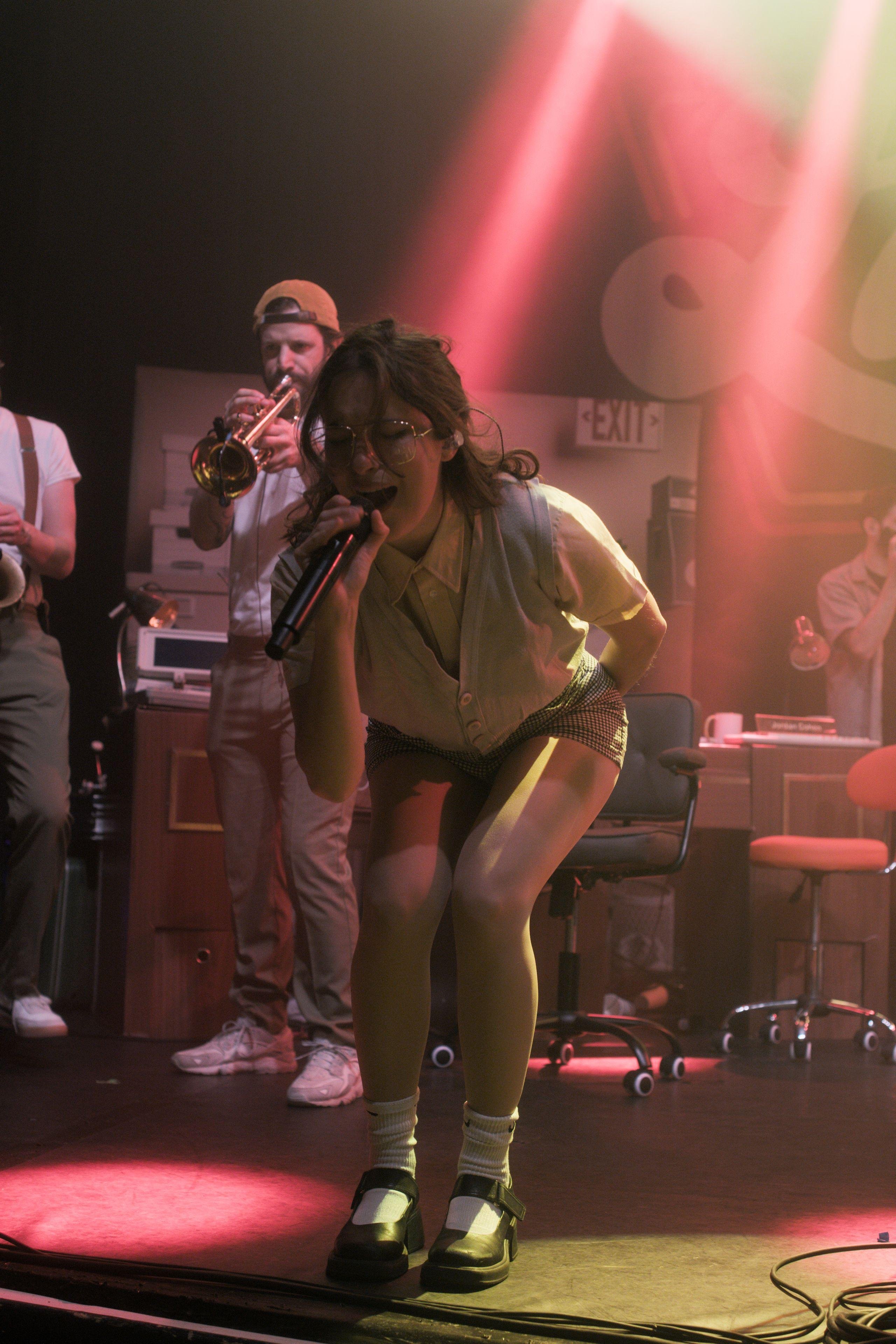 Photo verticale. Gracie Lawrence sur scène poussant un cri dans le micro en se pliant en deux