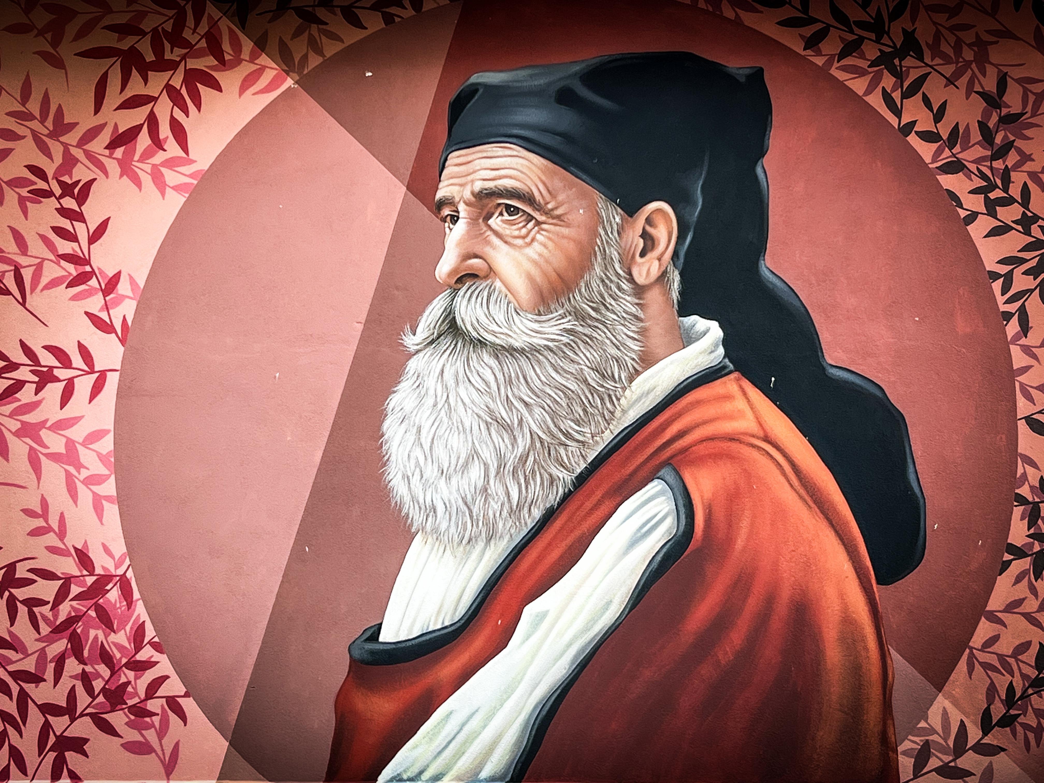 Murale di un uomo anziano con una lunga barba bianca e vestito con abiti tradizionali. Lo sfondo ha un design circolare con tonalità rosa e motivi di fogliame.