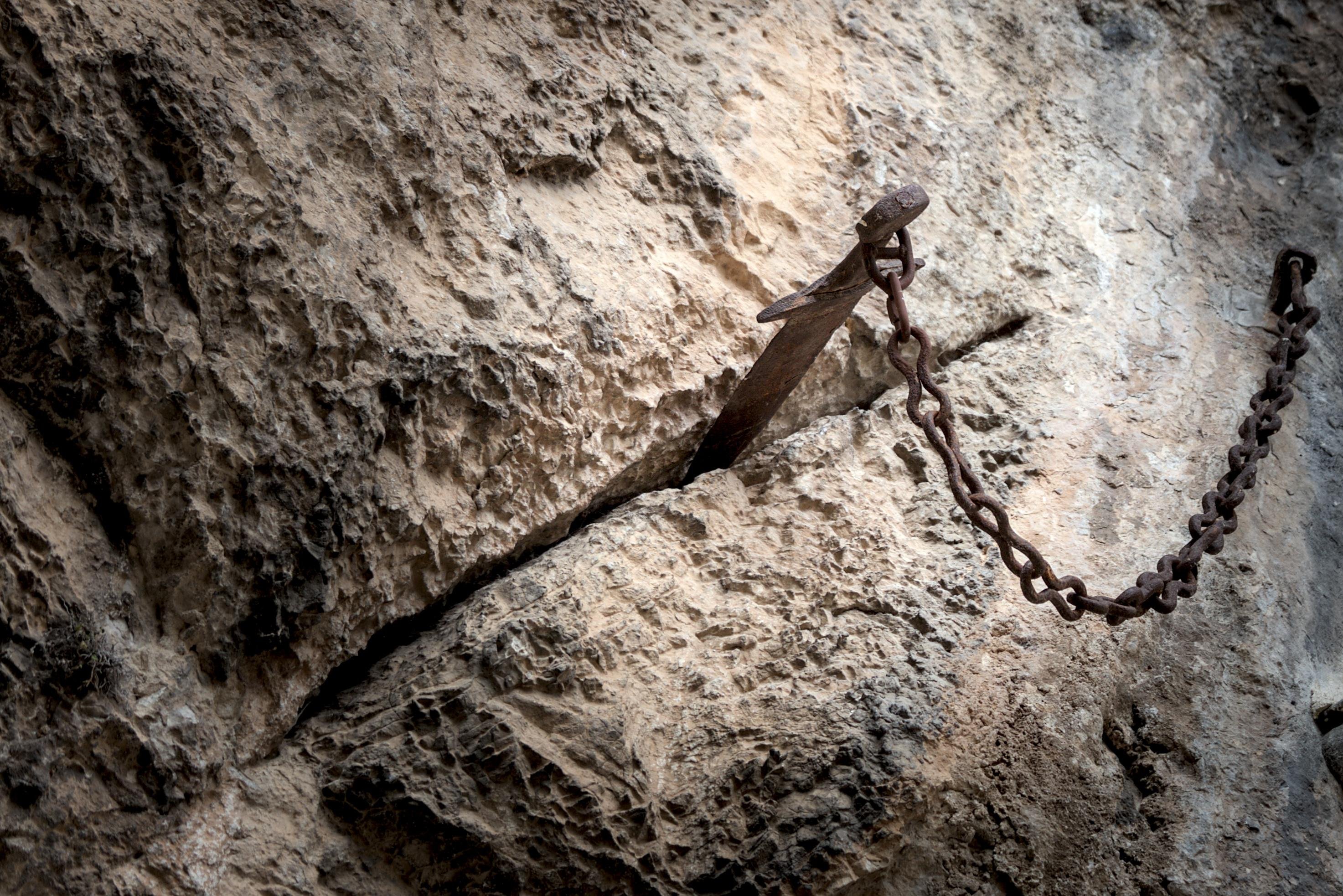 une épée rouillée pas les âges fichée dans un mur de roche, et attachée à une chaîne