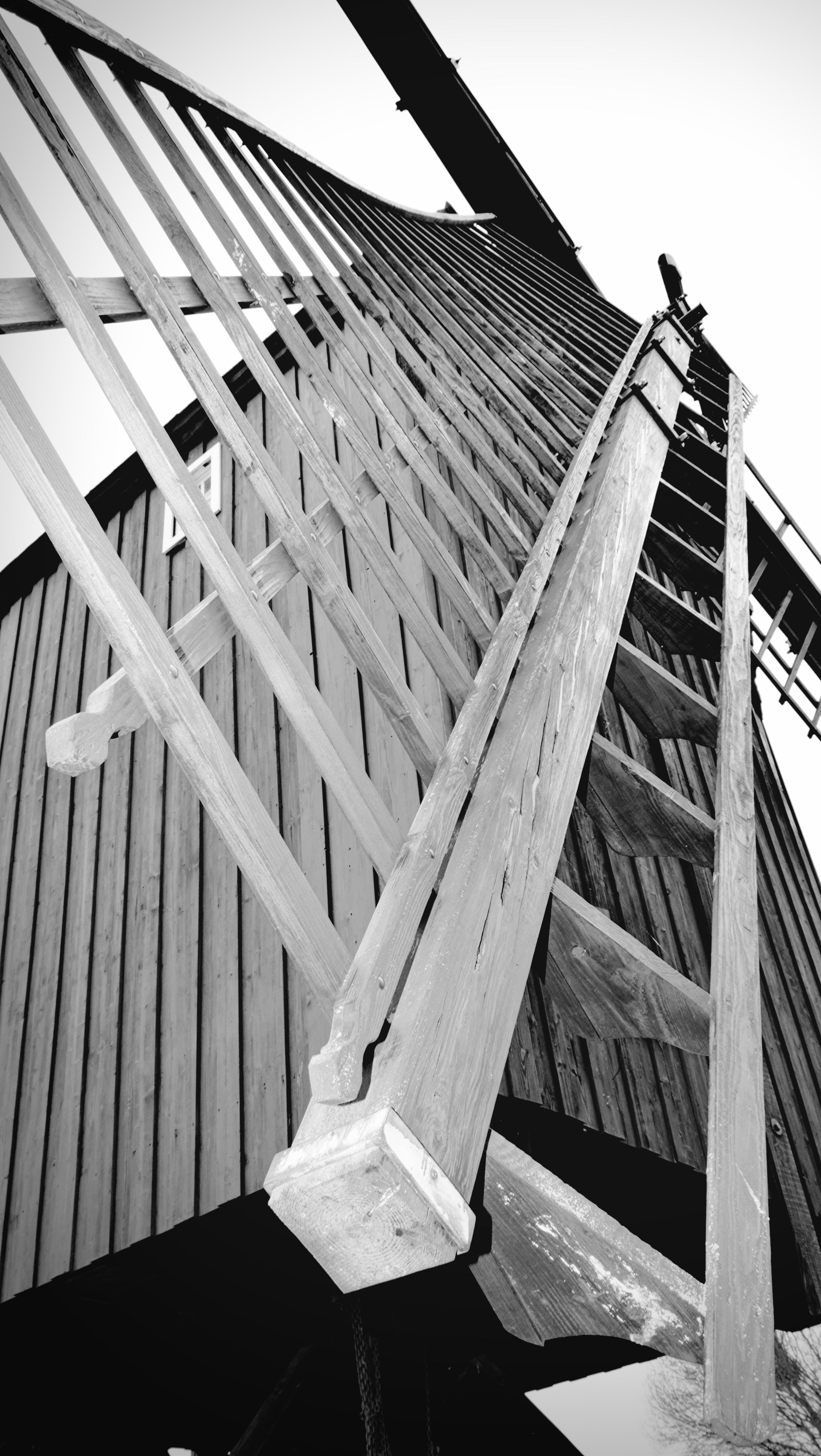 This image shows a close-up view of a windmill, specifically focusing on the wooden blades or sails and the structure surrounding them. The perspective gives an upward angle, highlighting the intricate construction and texture of the wood.